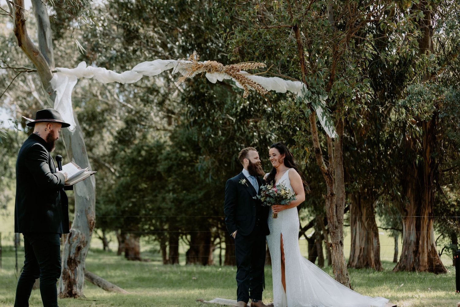 Bride and groom standing under a rustic floral archway during a bushland wedding ceremony in Melbourne with a celebrant.