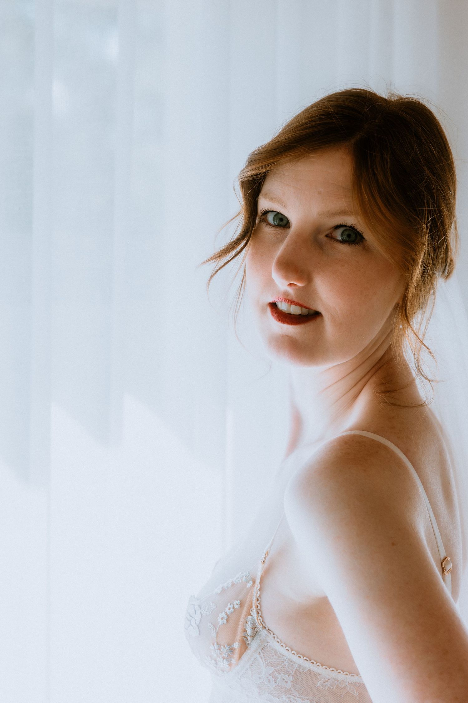 Soft bridal portrait of a woman in white lace lingerie with a wedding veil, highlighting elegant bridal boudoir photography.