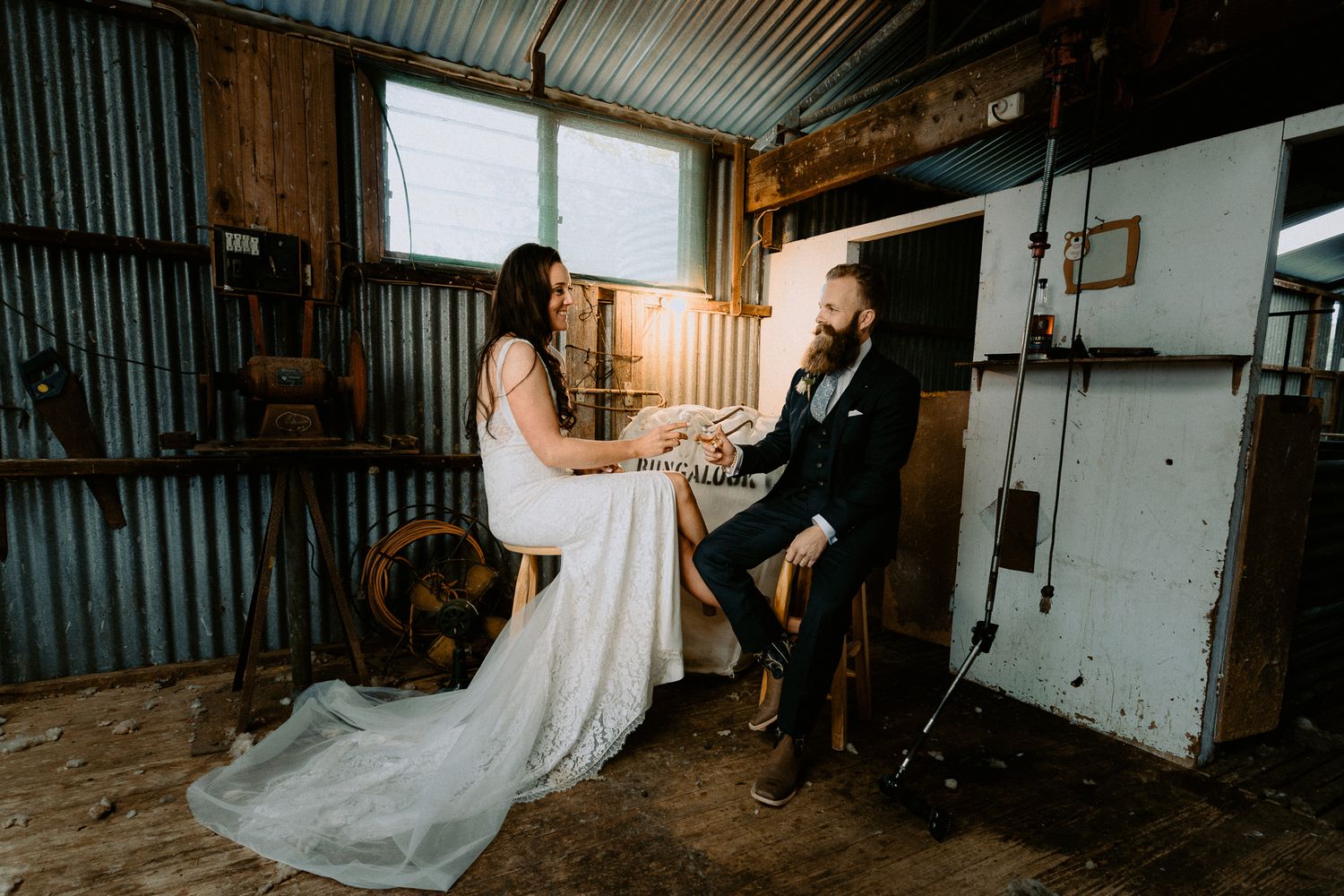 Bride and groom sharing a whiskey toast inside a rustic, industrial corrugated iron shed during their wedding reception.