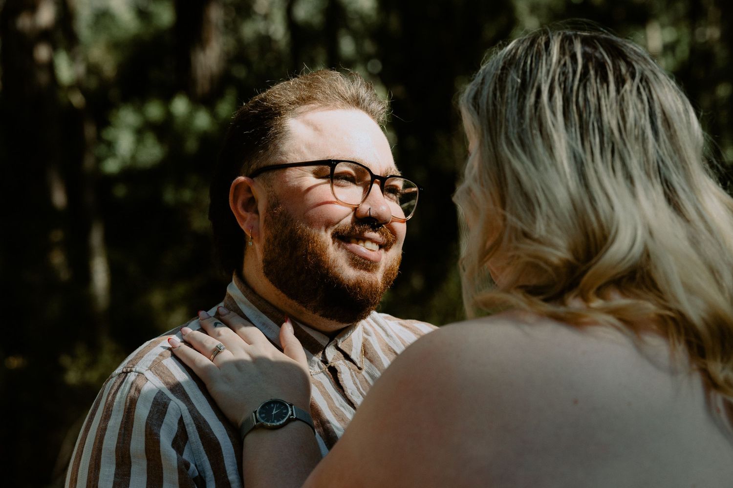 Close-up portrait of a groom-to-be smiling at his partner during an outdoor forest engagement session.