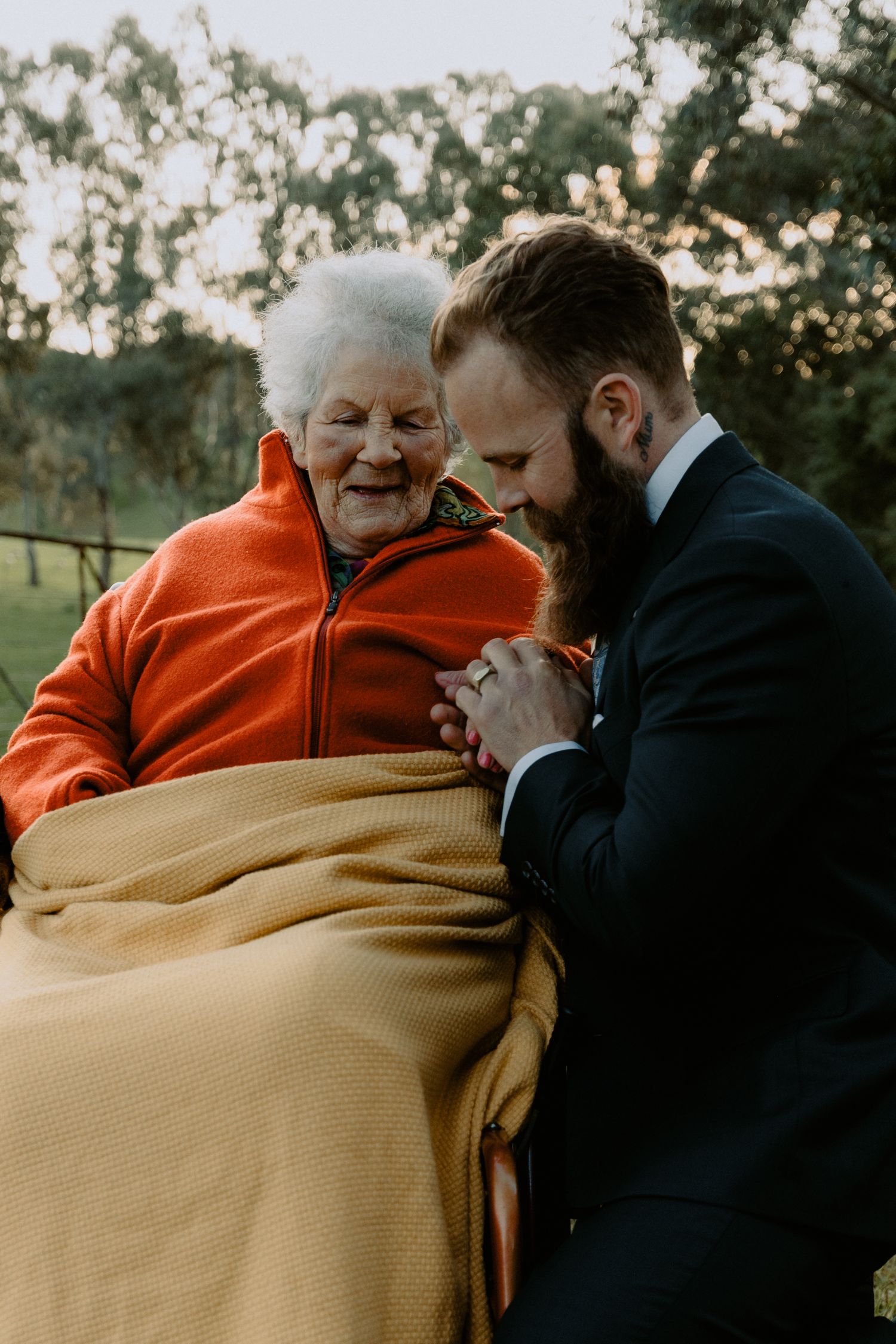 Emotional candid wedding moment of a groom holding the hand of an elderly family member during an outdoor reception.