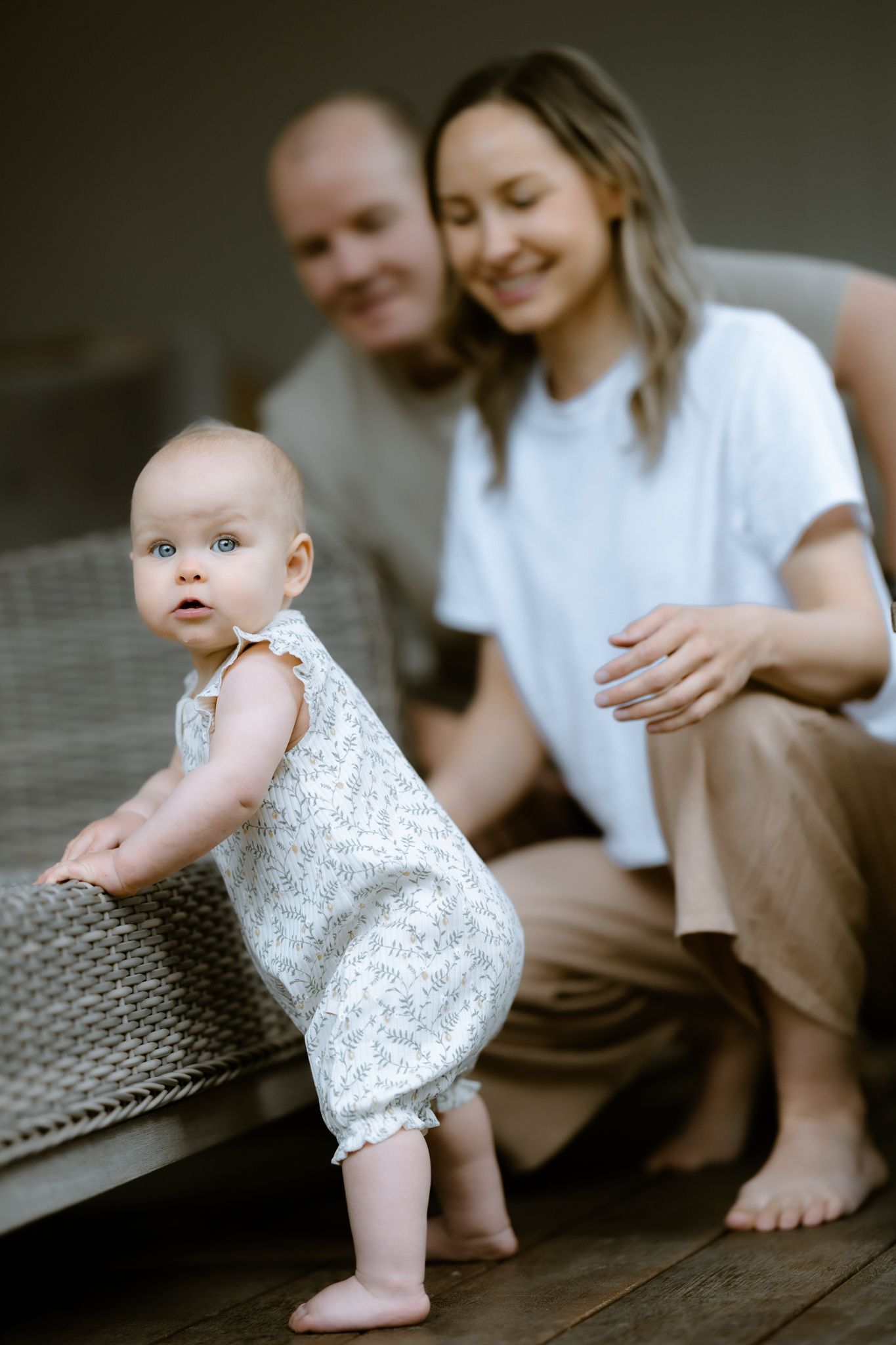 Shallow focus shot of a baby girl learning to stand on a deck with parents blurred in the background, Melbourne lifestyle photography