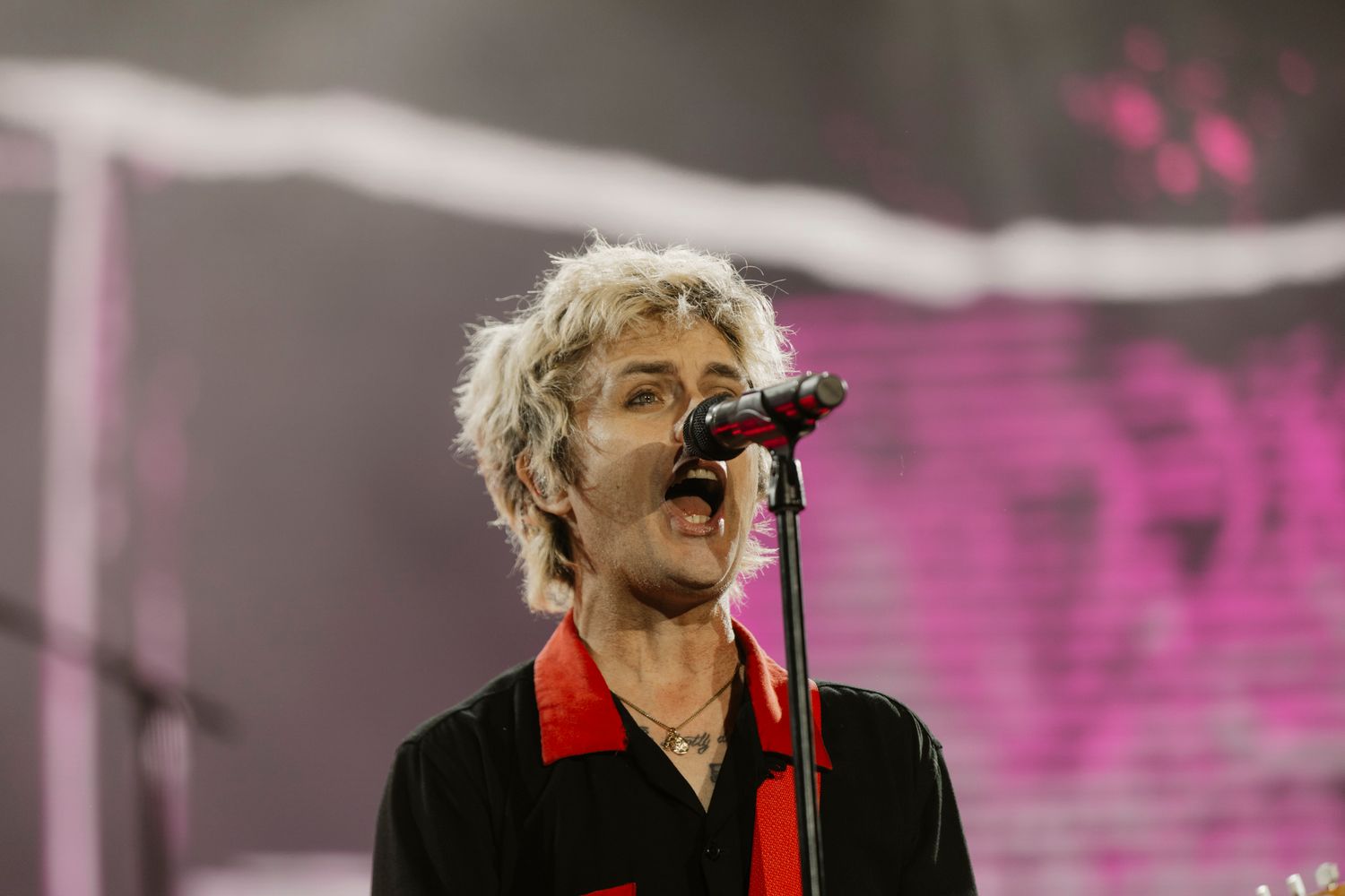 Close-up of Billie Joe Armstrong singing at a Green Day stadium tour. Expressive rock music portrait with vibrant pink stage visuals.
