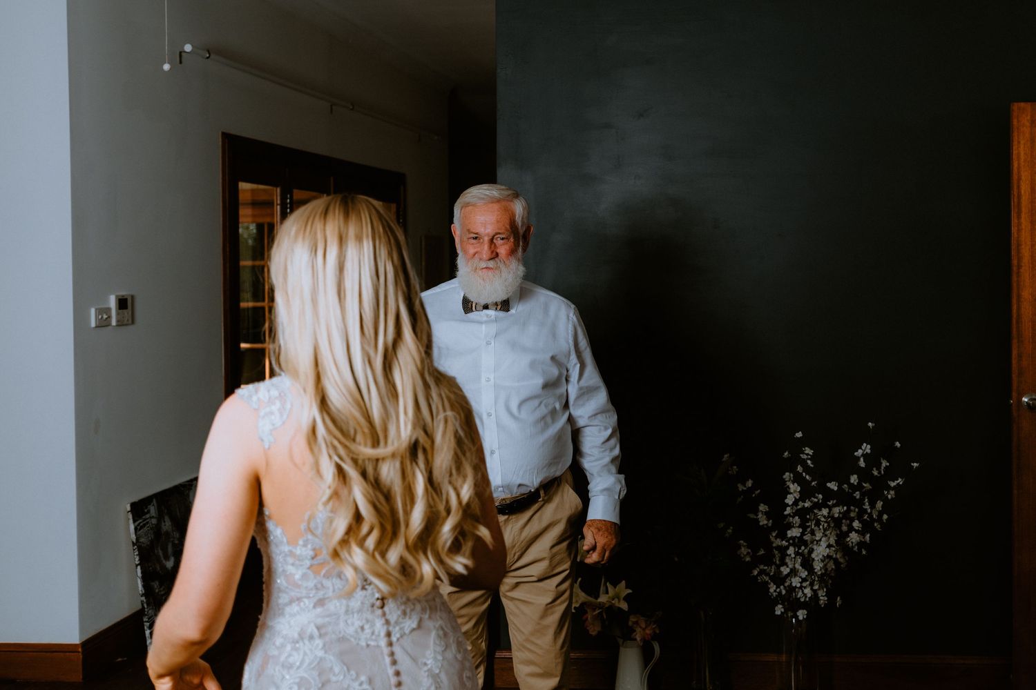 Emotional first look between a blonde bride in a lace wedding dress and her father before the ceremony.