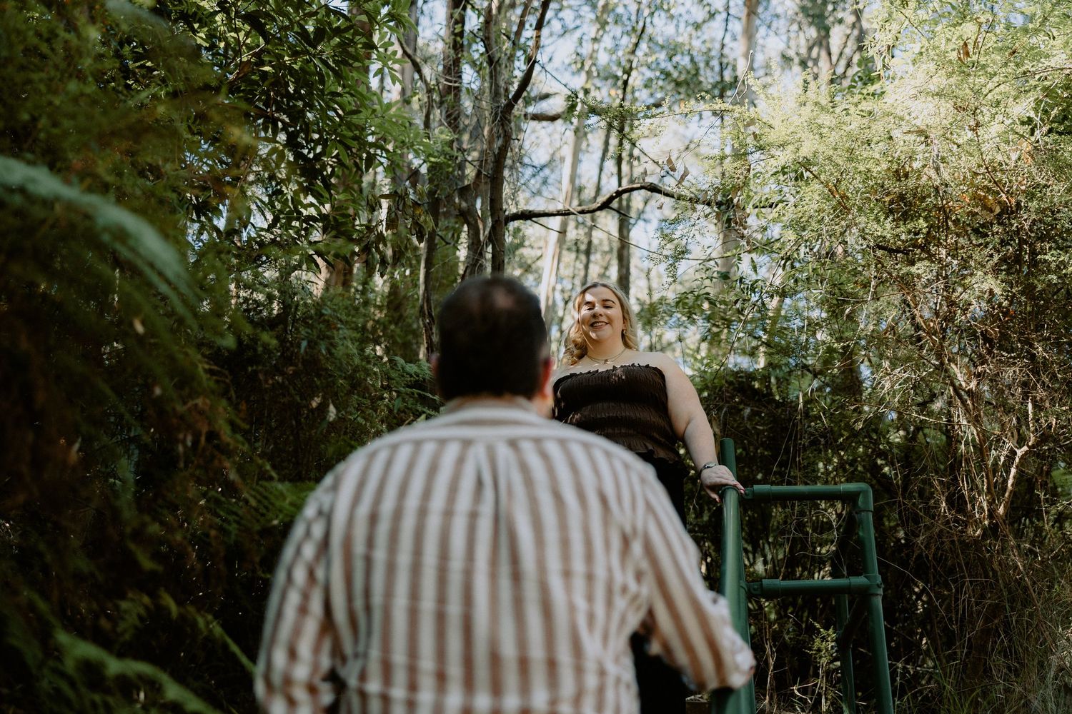 Candid forest engagement photoshoot featuring a couple on a wooded trail with a rustic, natural aesthetic.