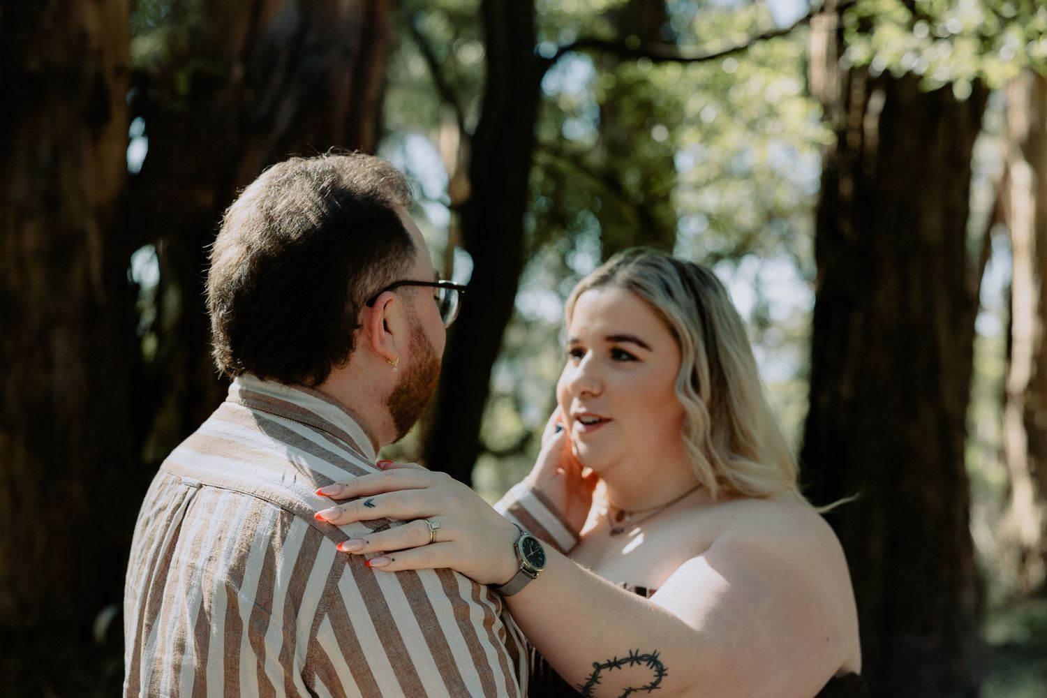 Intimate engagement photoshoot portrait of a couple sharing a quiet moment in a sun-drenched forest.