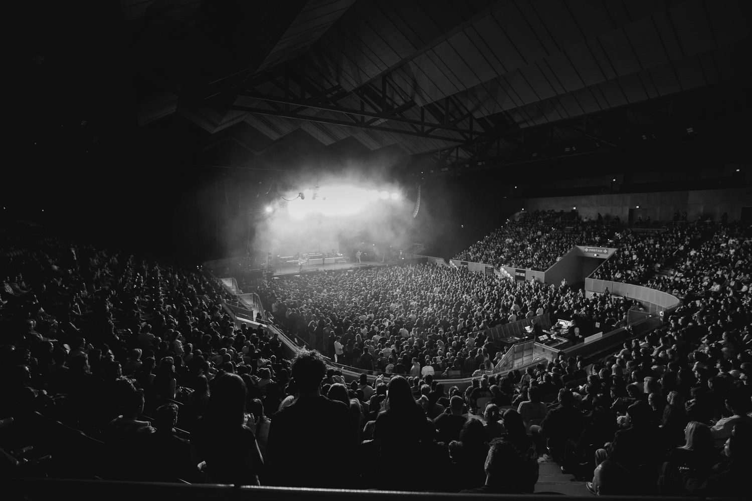 Wide-angle black and white interior of a crowded Melbourne Margaret Court arena concert venue during a live music event.