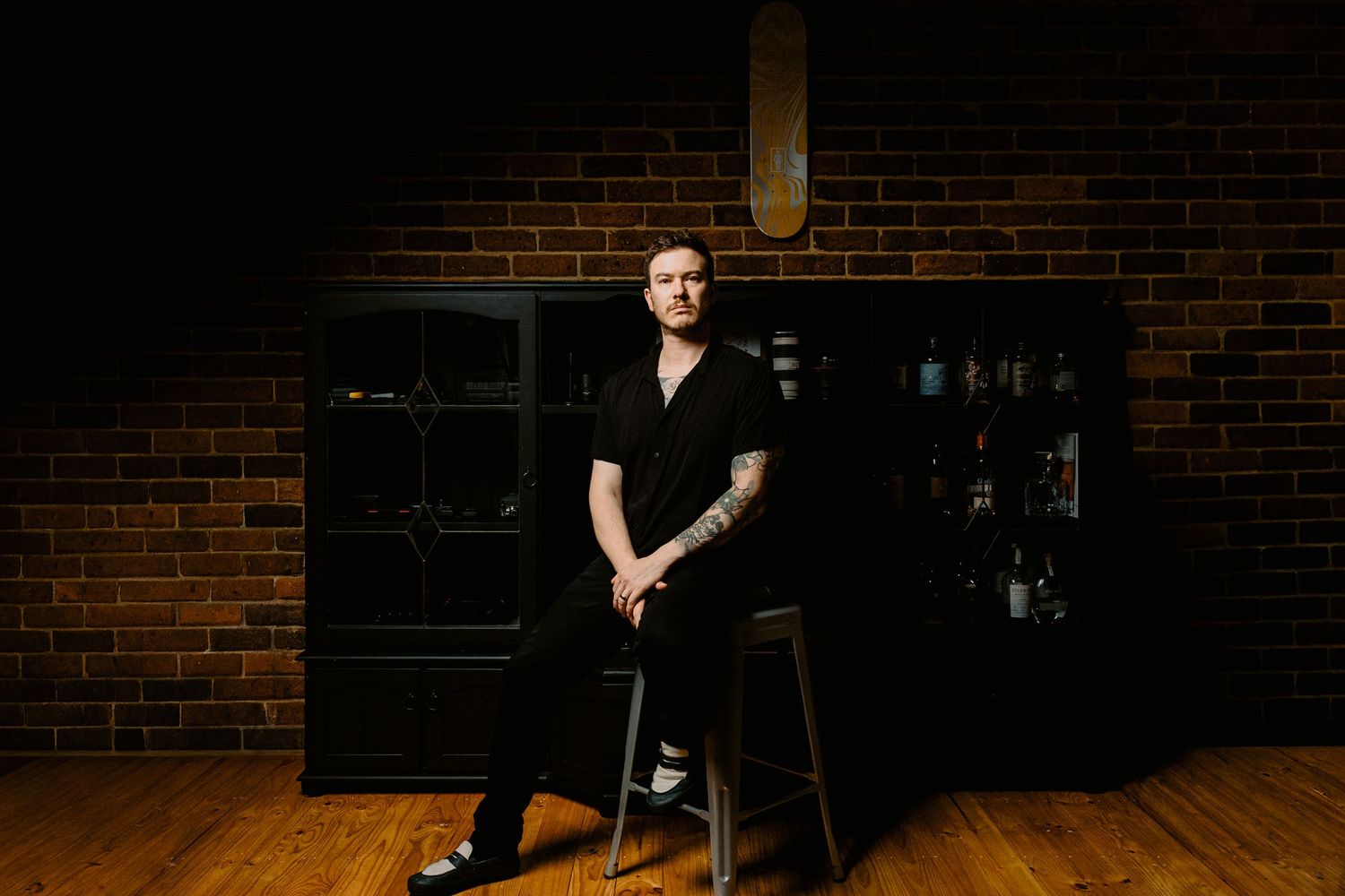 Full length shot of a Melbourne-based creative photographer sitting in a dark, atmospheric studio space.