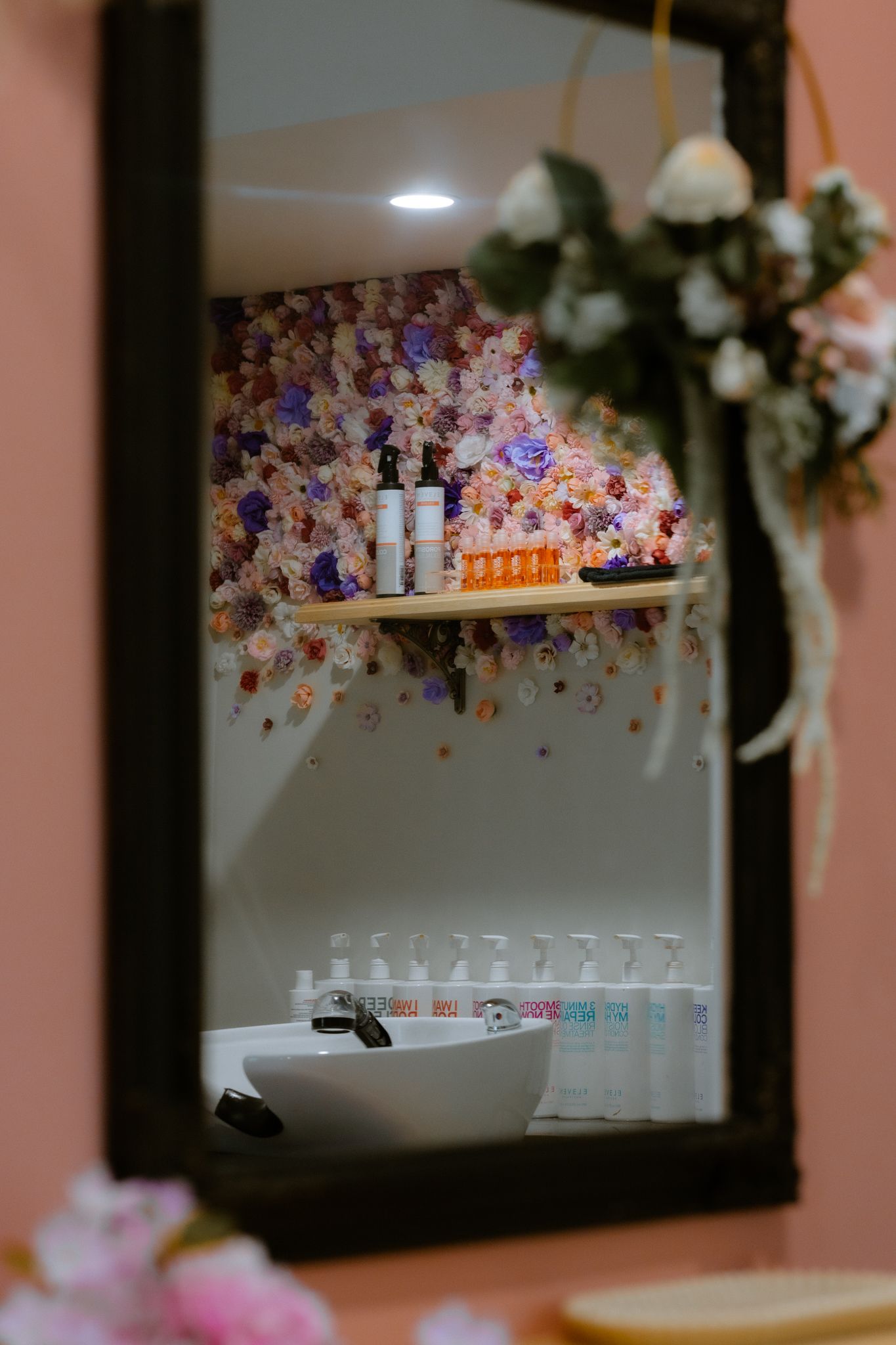 Artistic lifestyle photography of a hair salon wash station reflected in a mirror with a floral wall background.