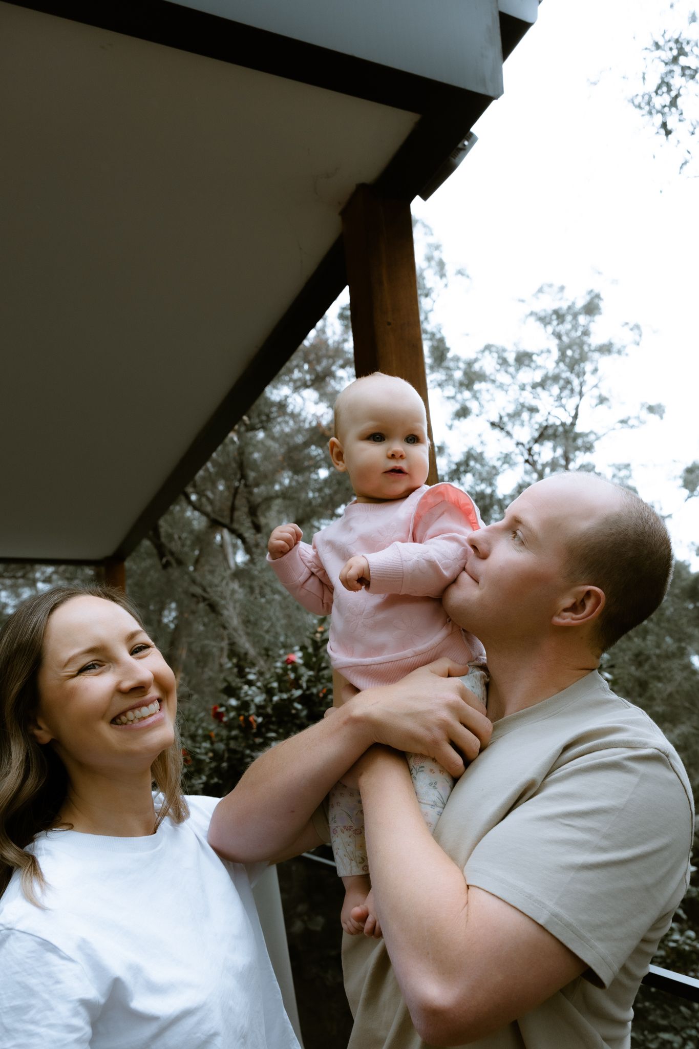 Candid lifestyle photography of a mother and father holding their baby girl outdoors, natural light family session Melbourne.