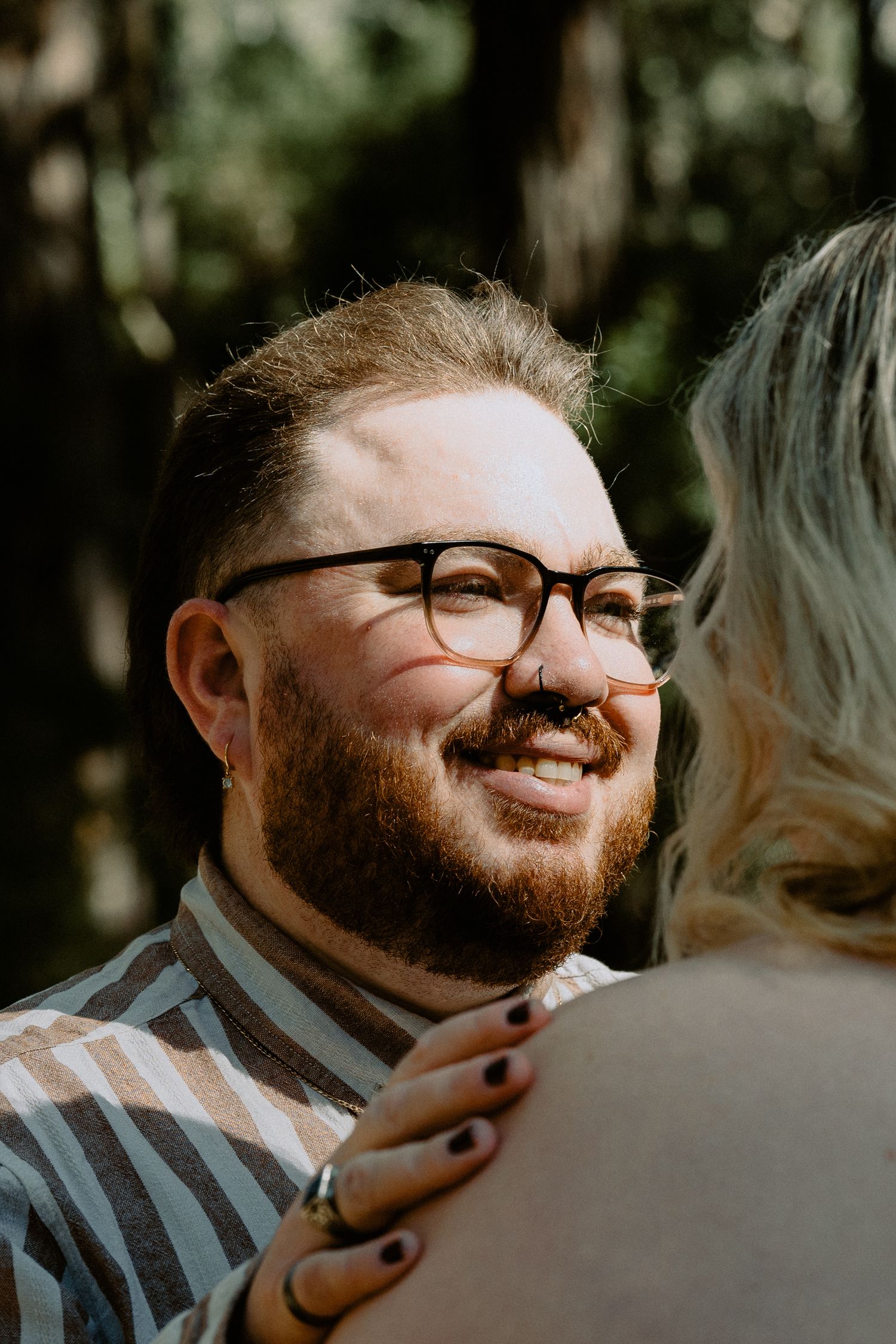 Close-up portrait of a groom-to-be smiling at his partner during an outdoor forest engagement session.