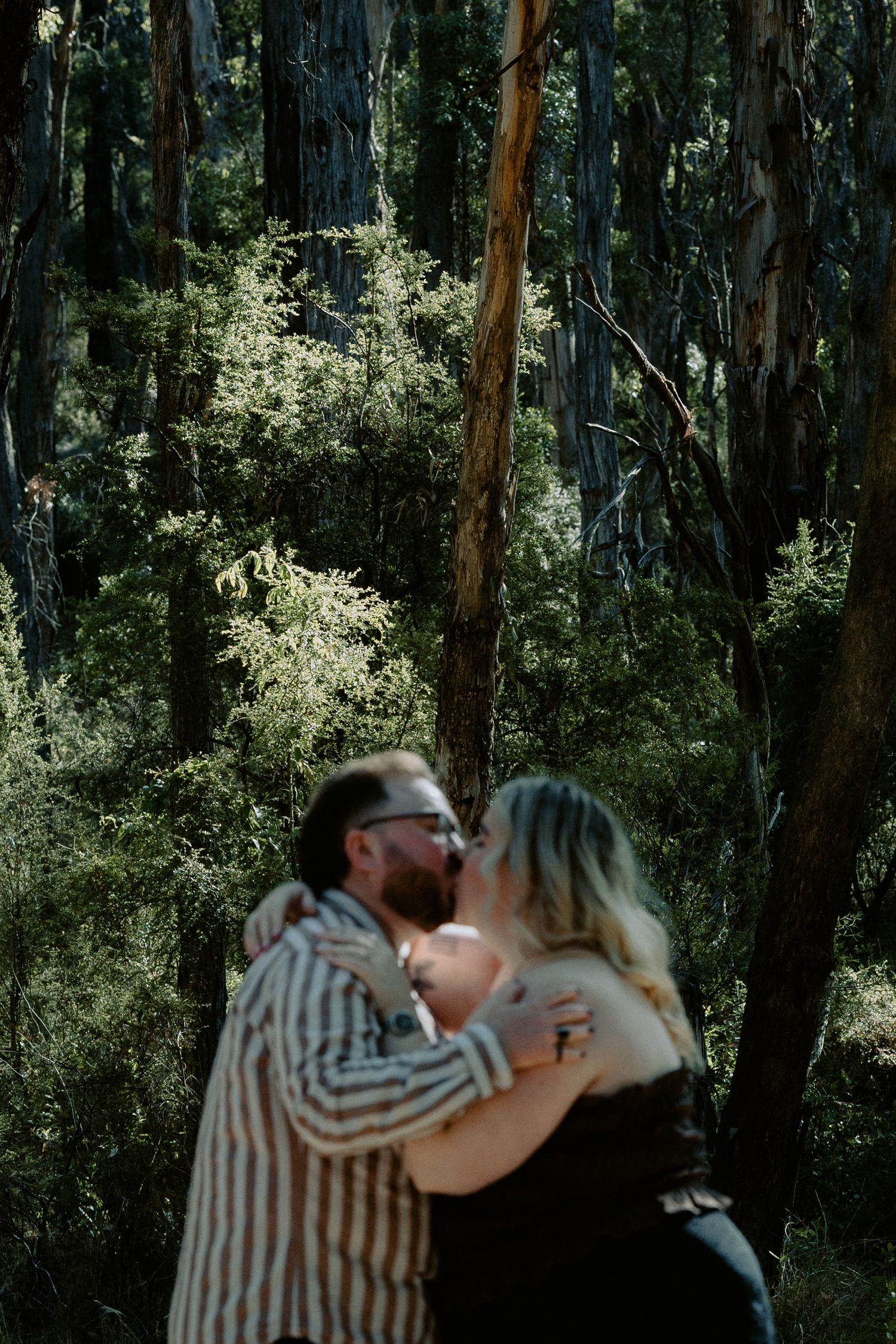Romantic blurred-motion kiss between a newly engaged couple during a rustic outdoor session in the woods.