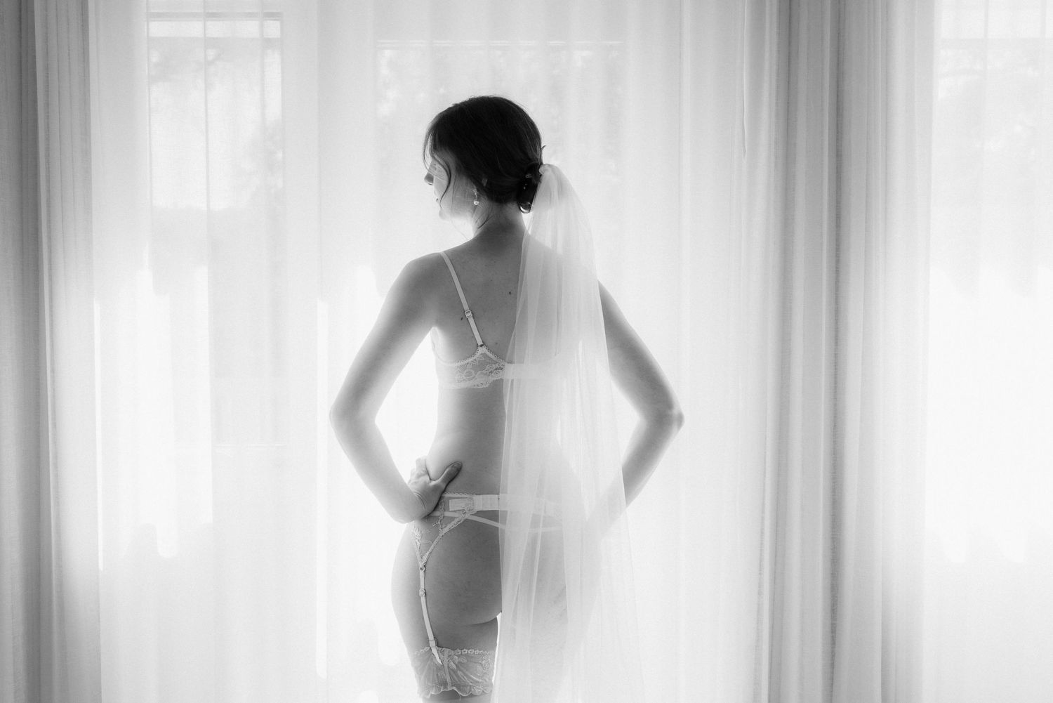 B&W silhouette of a bride in a veil and lingerie standing against a bright window, Melbourne wedding photography.