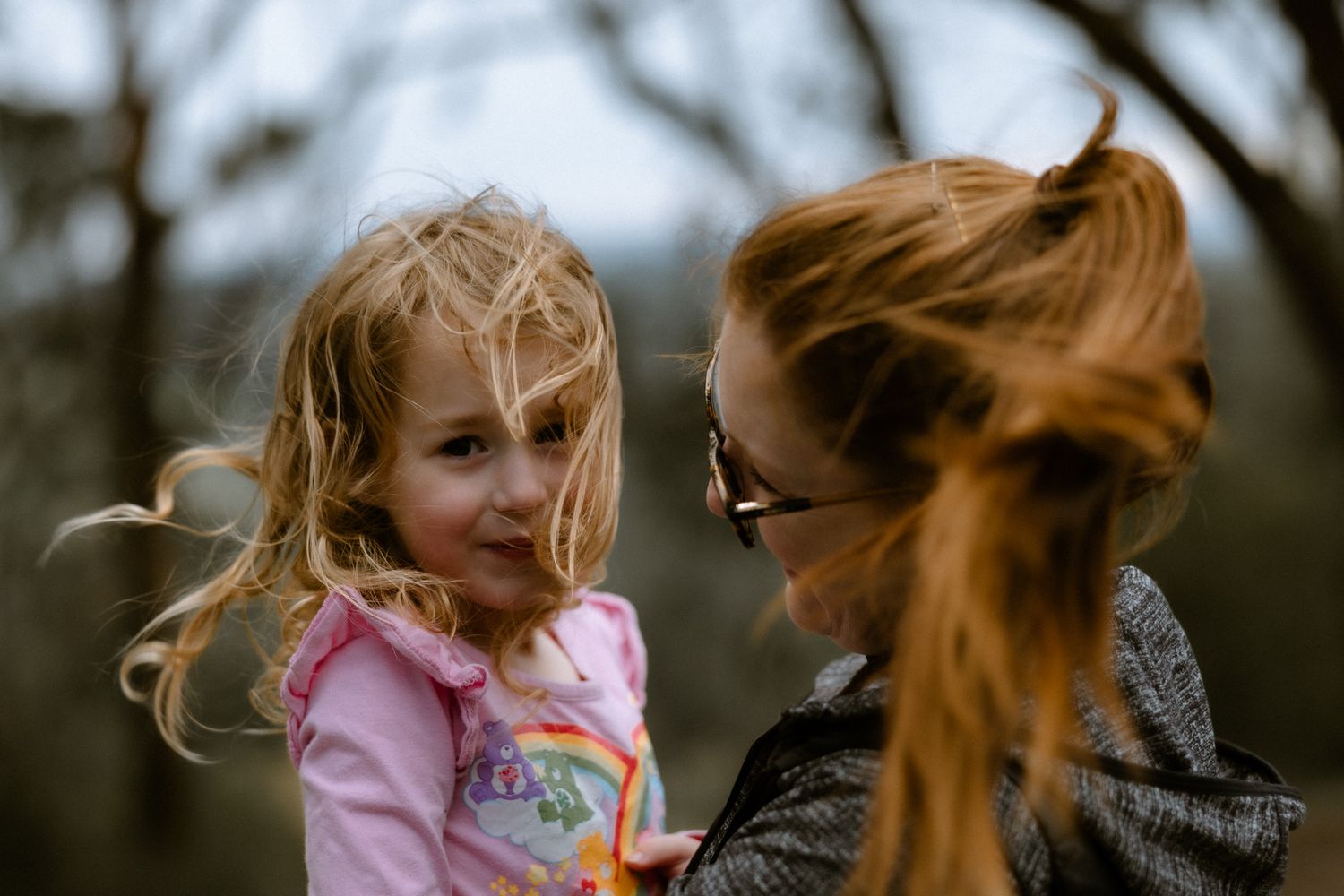 Candid lifestyle photography of a mother holding her young daughter with windblown hair during an outdoor family session.