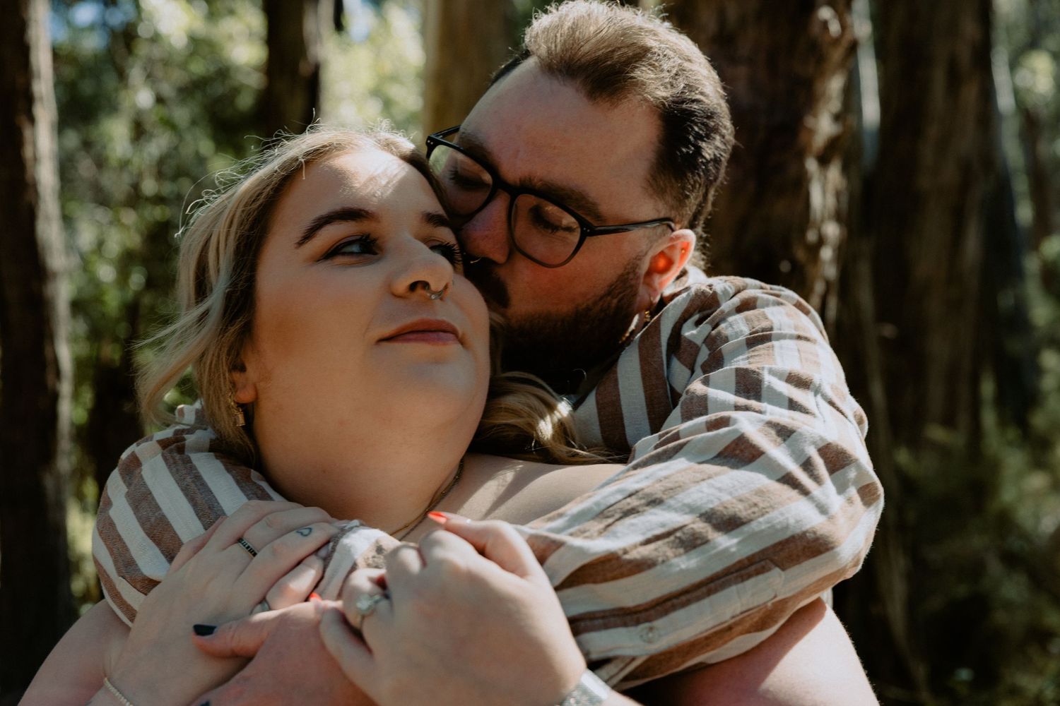 Intimate engagement photoshoot portrait of a couple sharing a quiet moment in a sun-drenched forest.
