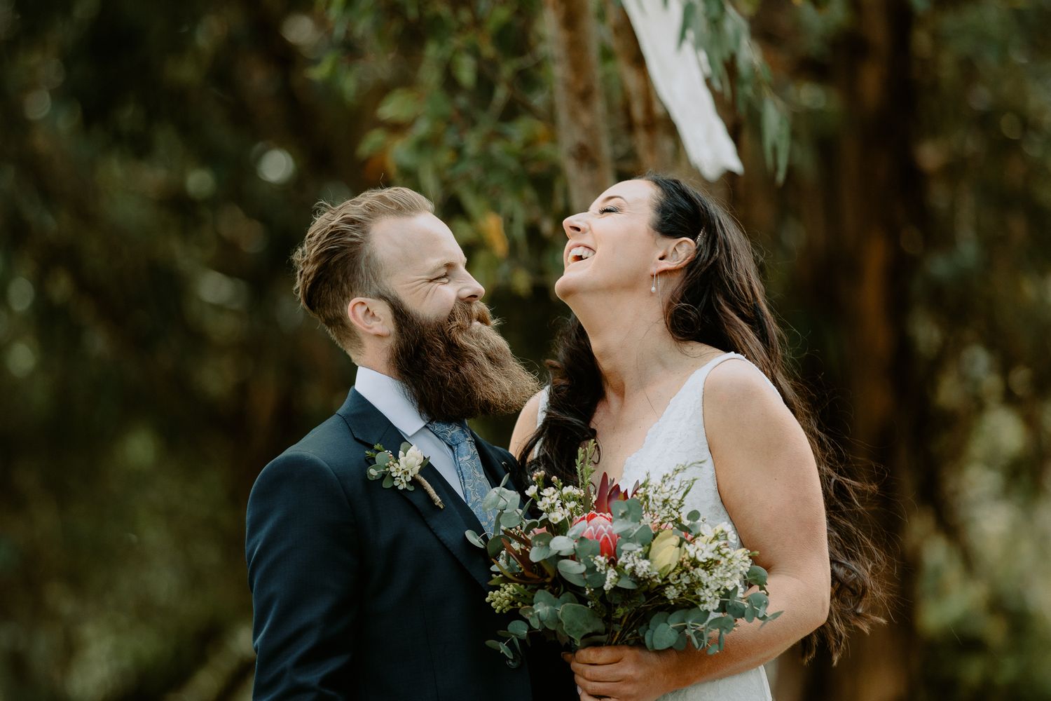 Candid wedding photography of a bride laughing joyfully while holding a native Australian floral bouquet next to the groom.