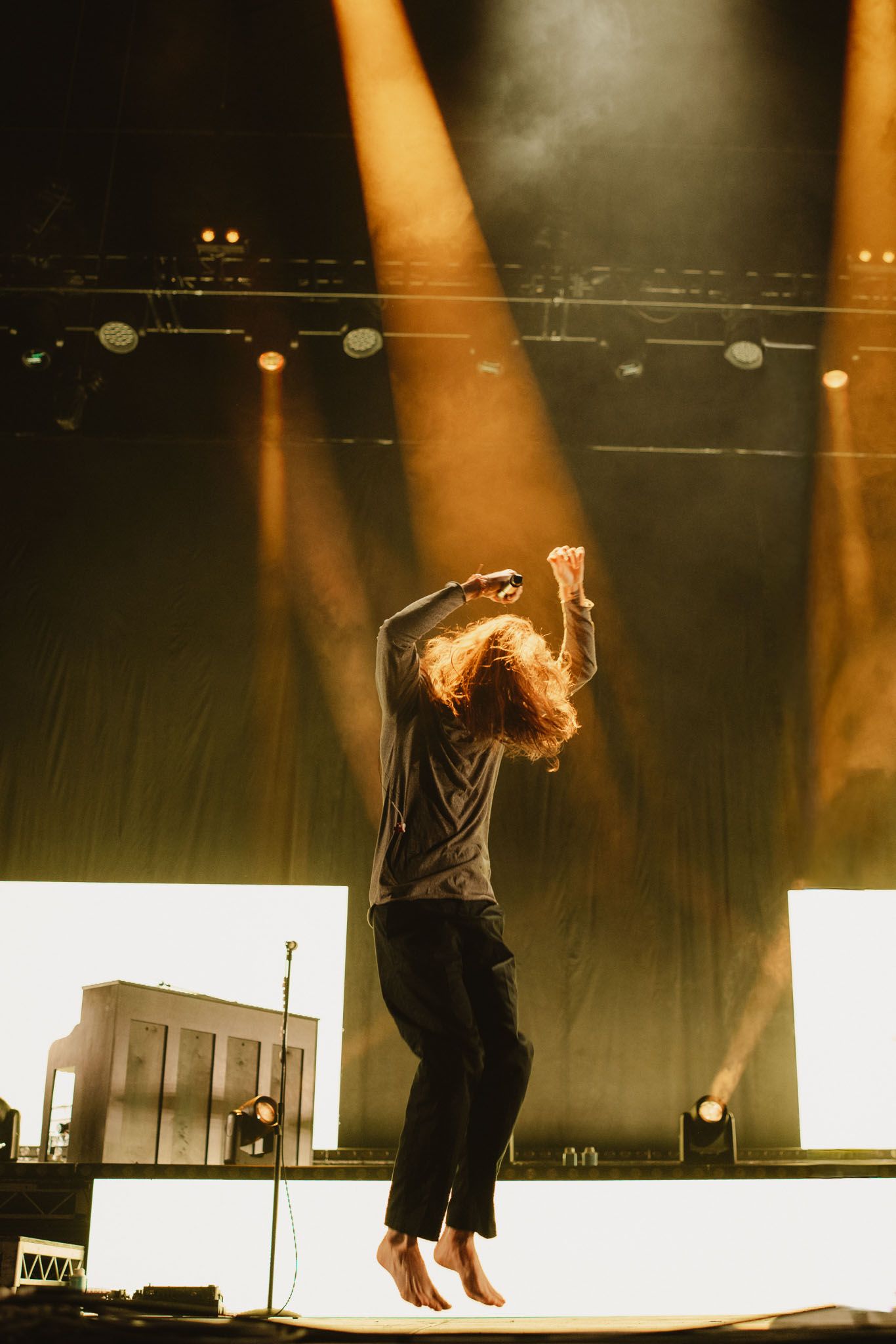 Mid-air jump of a vocalist during a live show. Action-packed concert photography featuring golden stage beams and high energy.