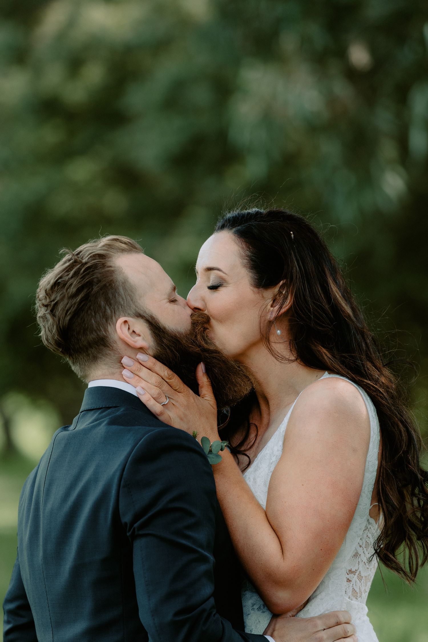 Close-up of a bride and groom's first kiss, showing the bride's lace dress and the groom's distinct beard at a Victorian wedding.