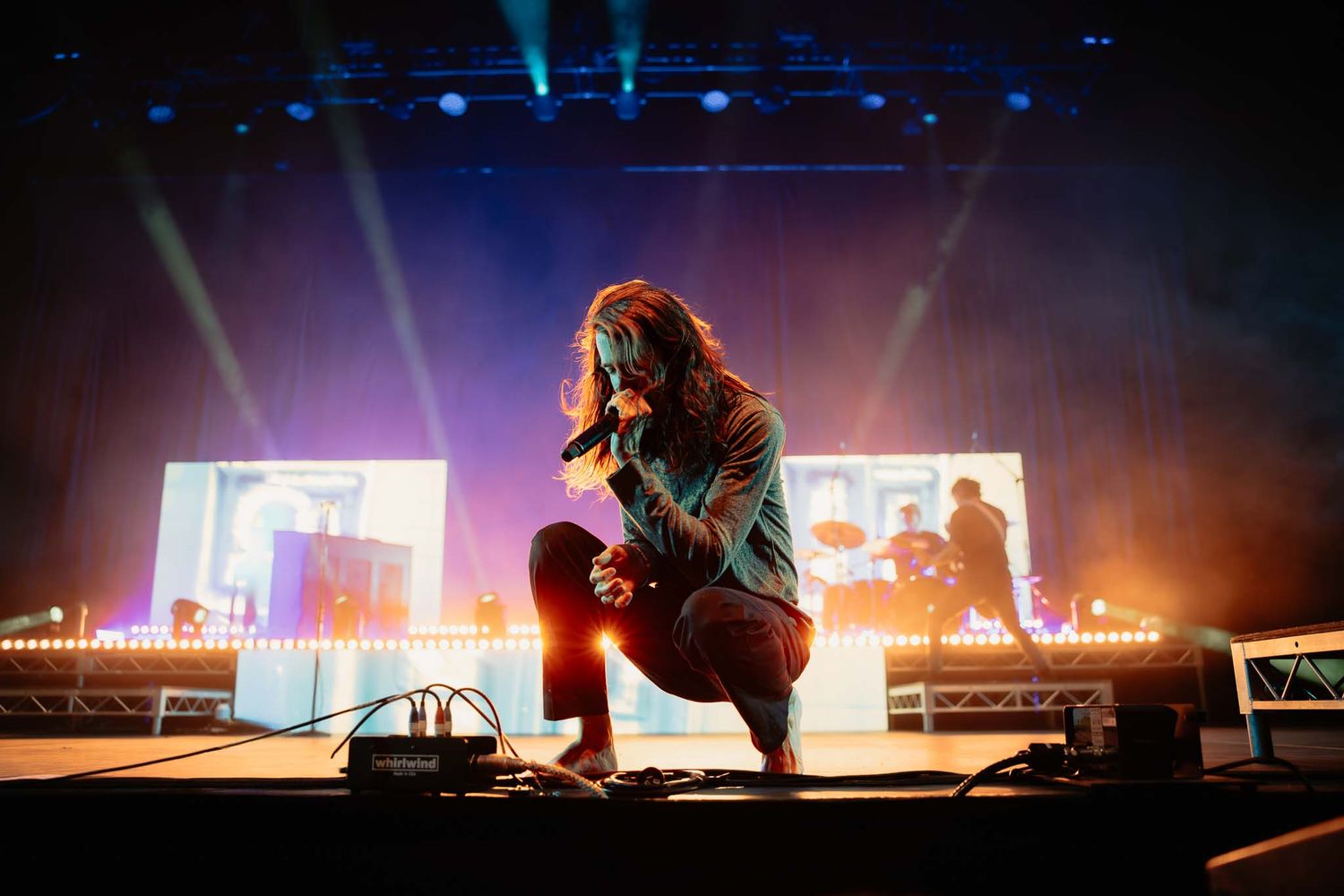 Atmospheric shot of a lead singer crouching on stage in hazy light. Artistic Melbourne concert photography with dramatic backlighting.