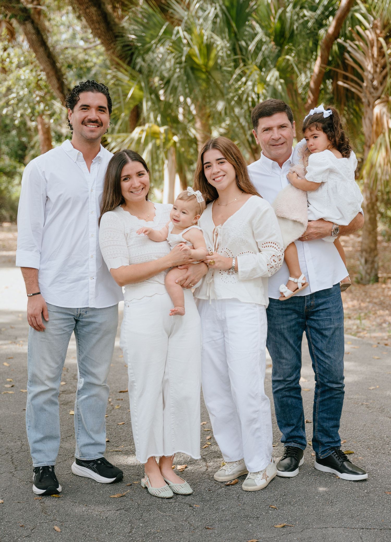 Family of six in white outfits posing together outdoors among tropical palm trees.