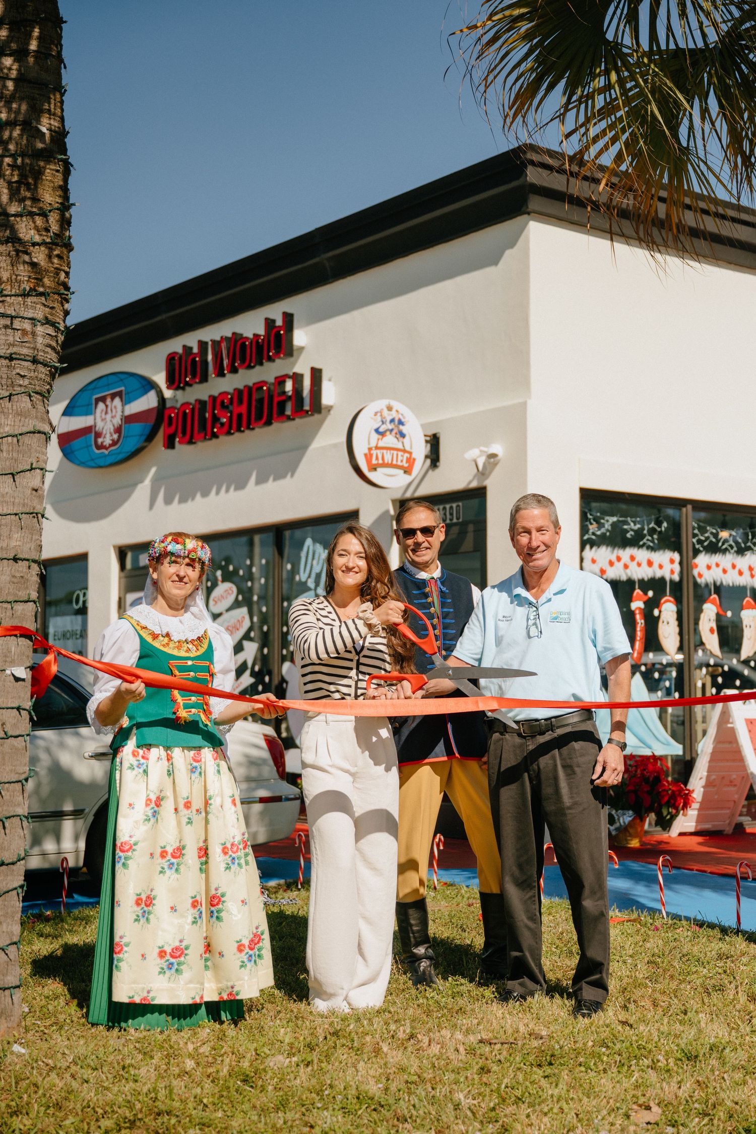 Ribbon cutting ceremony at Old World Polish Deli grand opening with four people in traditional and casual attire outdoors.