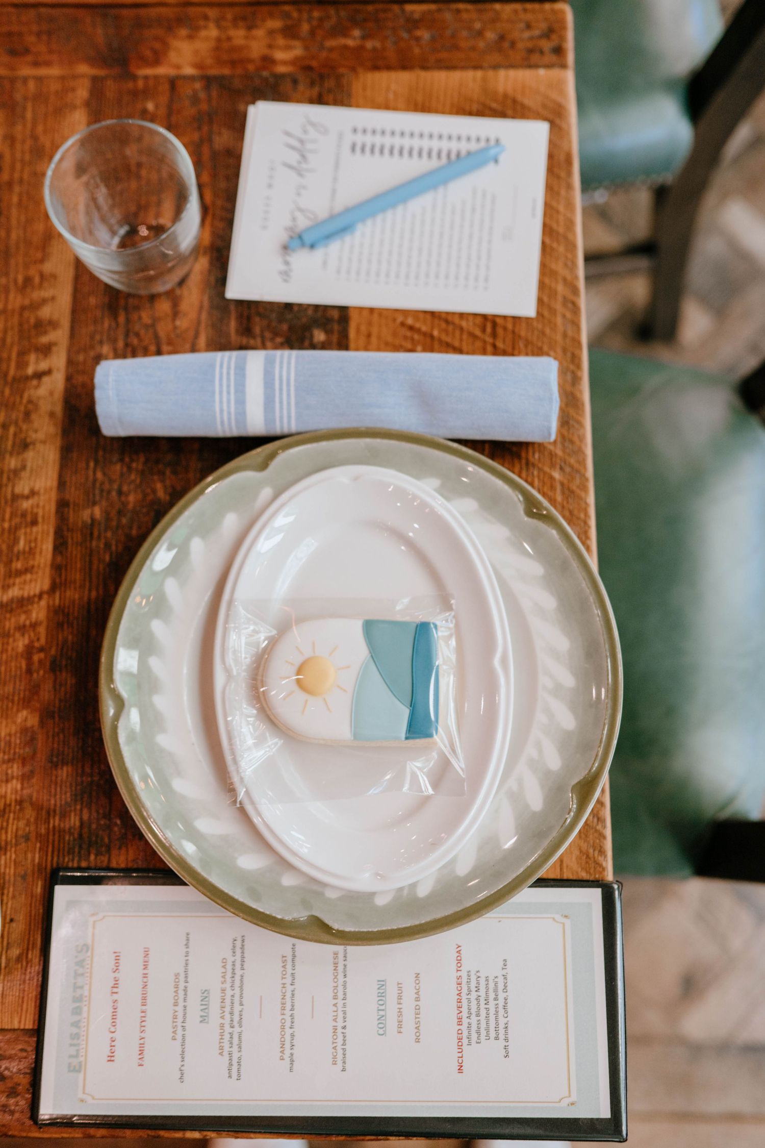 Baby shower table setting with green scalloped plate, wrapped cookie favor, blue napkin, and printed menu card.