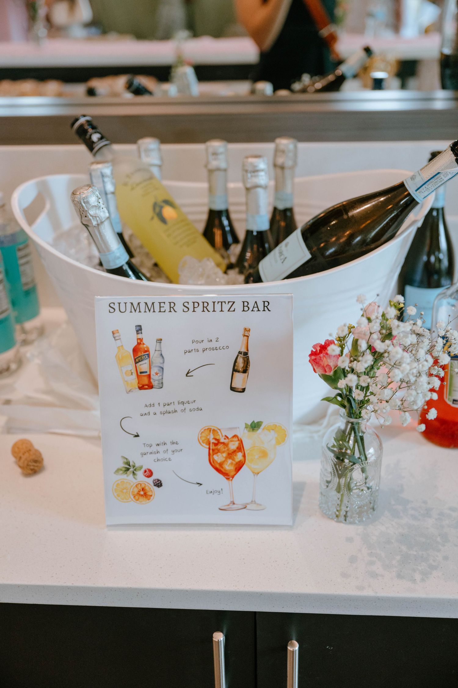 Summer Spritz Bar setup with chilled bottles, recipe sign, and floral arrangements.