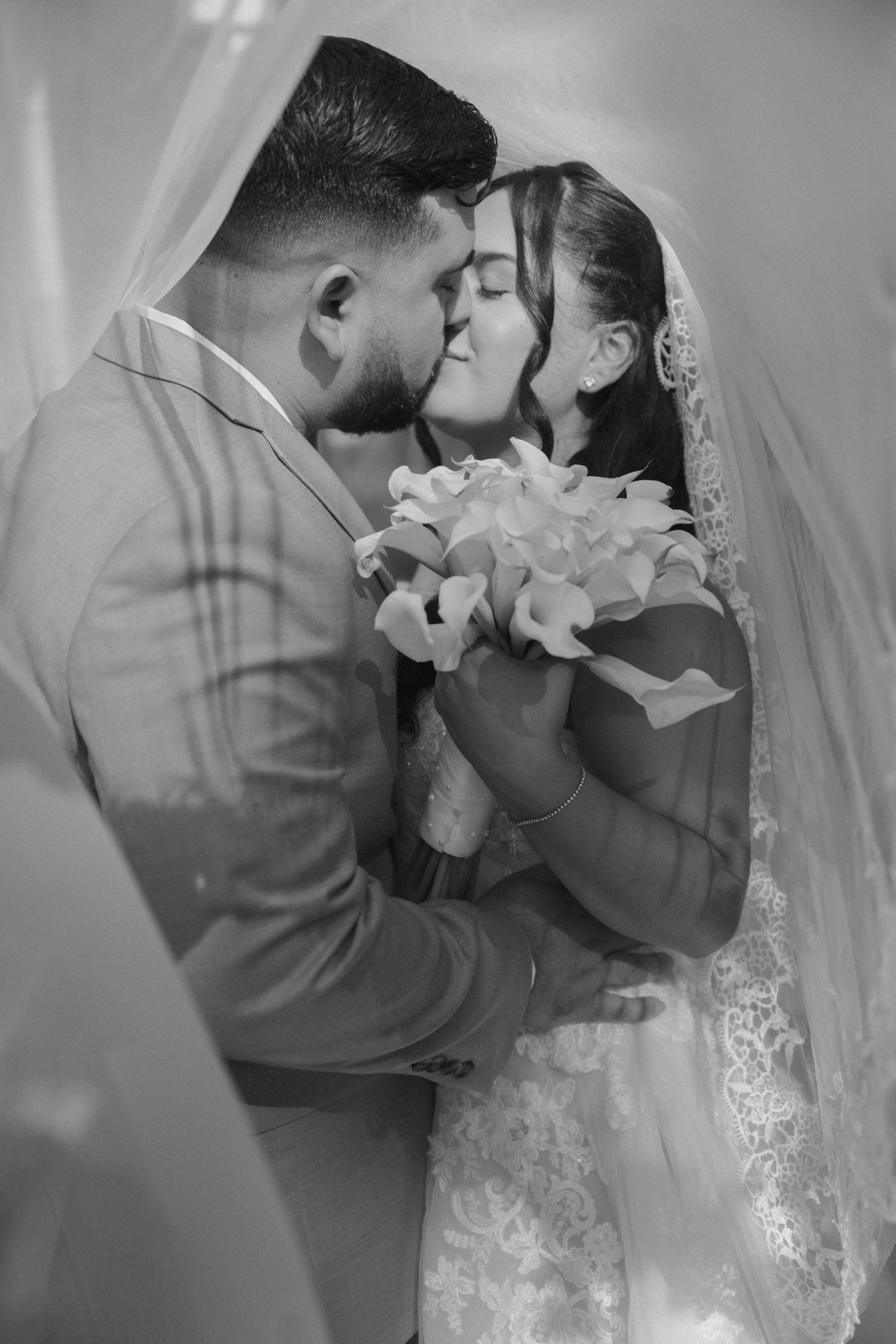 Black and white photo of bride and groom sharing a tender kiss under the wedding veil.