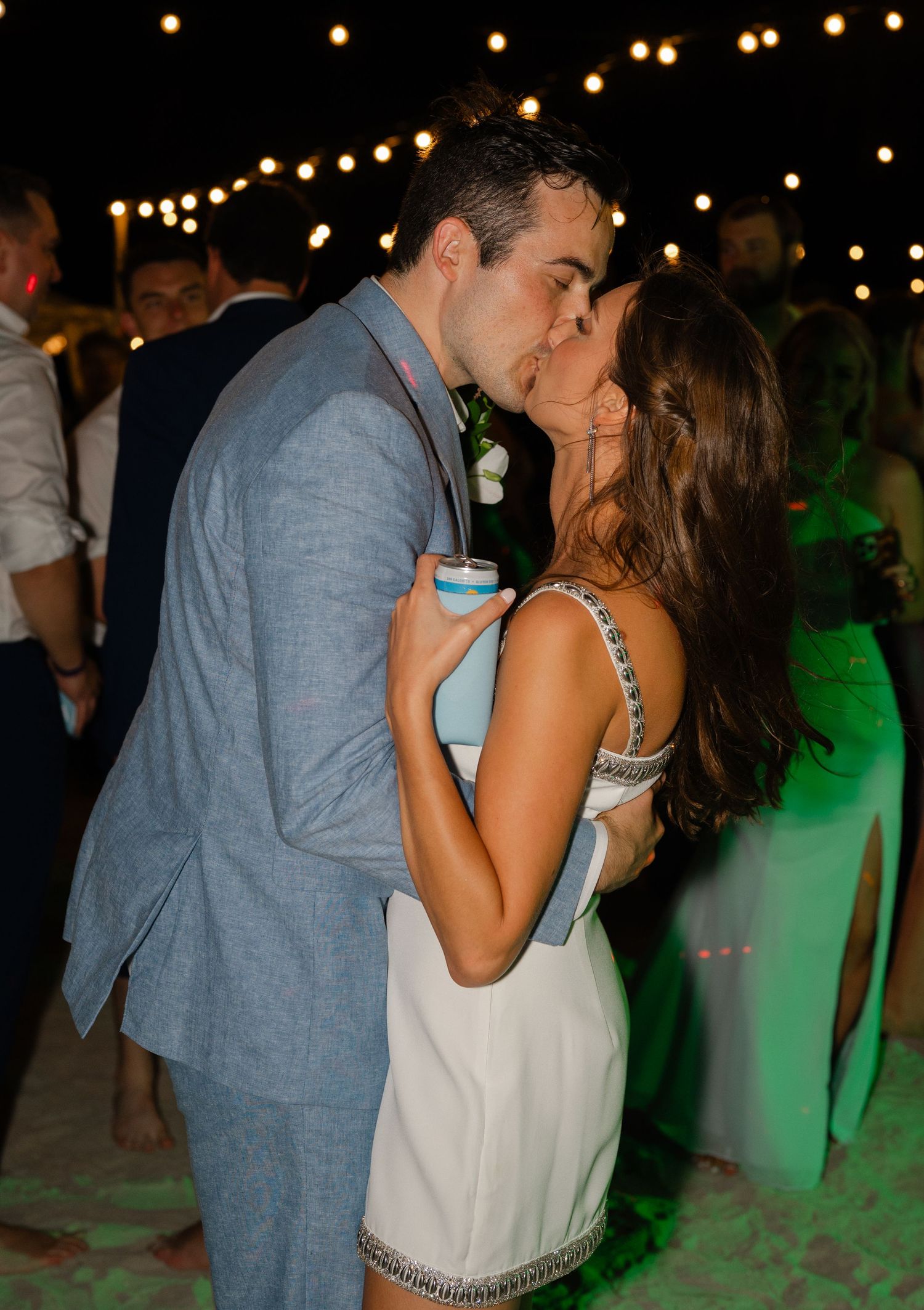 Couple sharing a romantic kiss on the dance floor at an outdoor wedding reception under string lights.