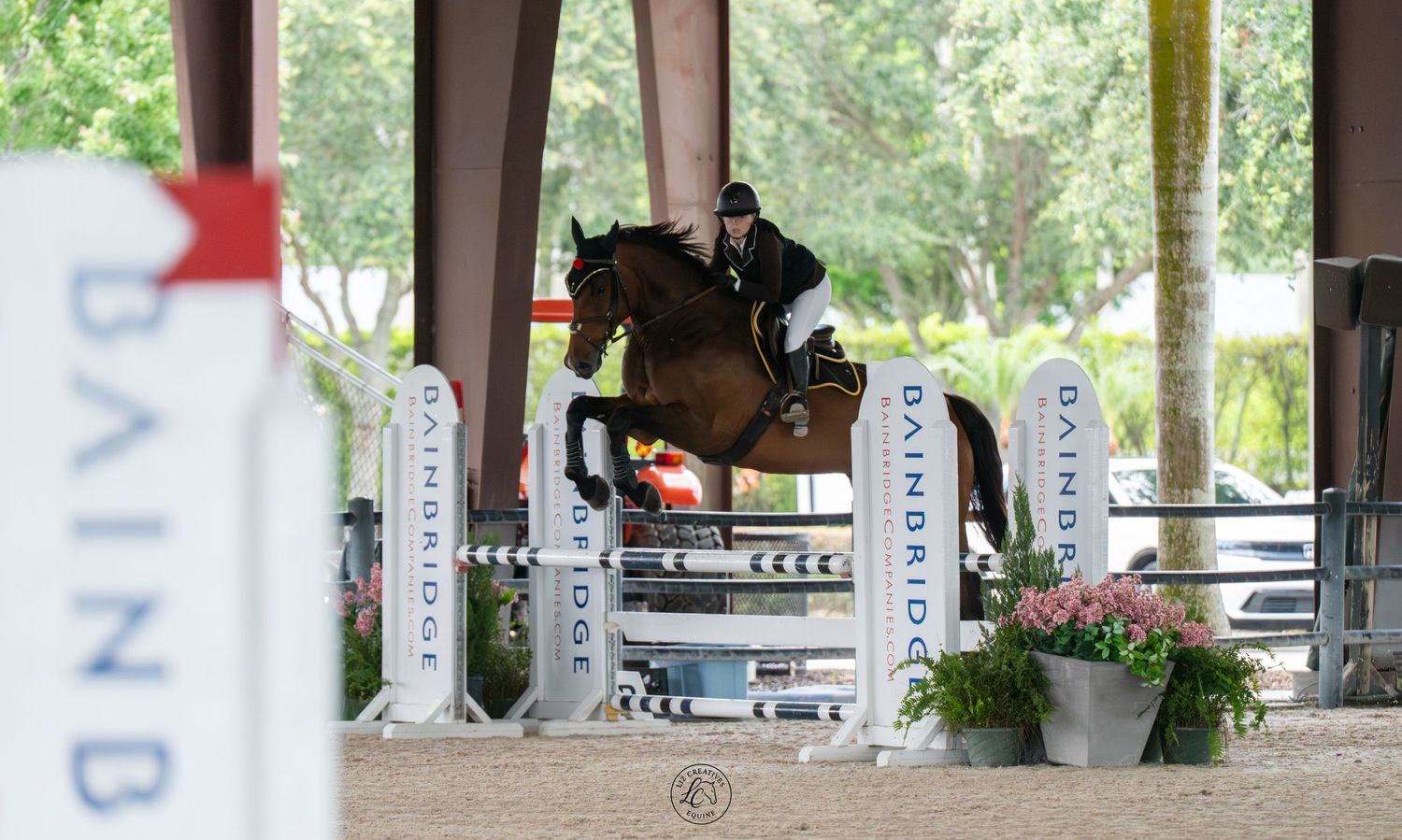 Equestrian rider on a brown horse jumping over a colorful fence at an outdoor show jumping competition.