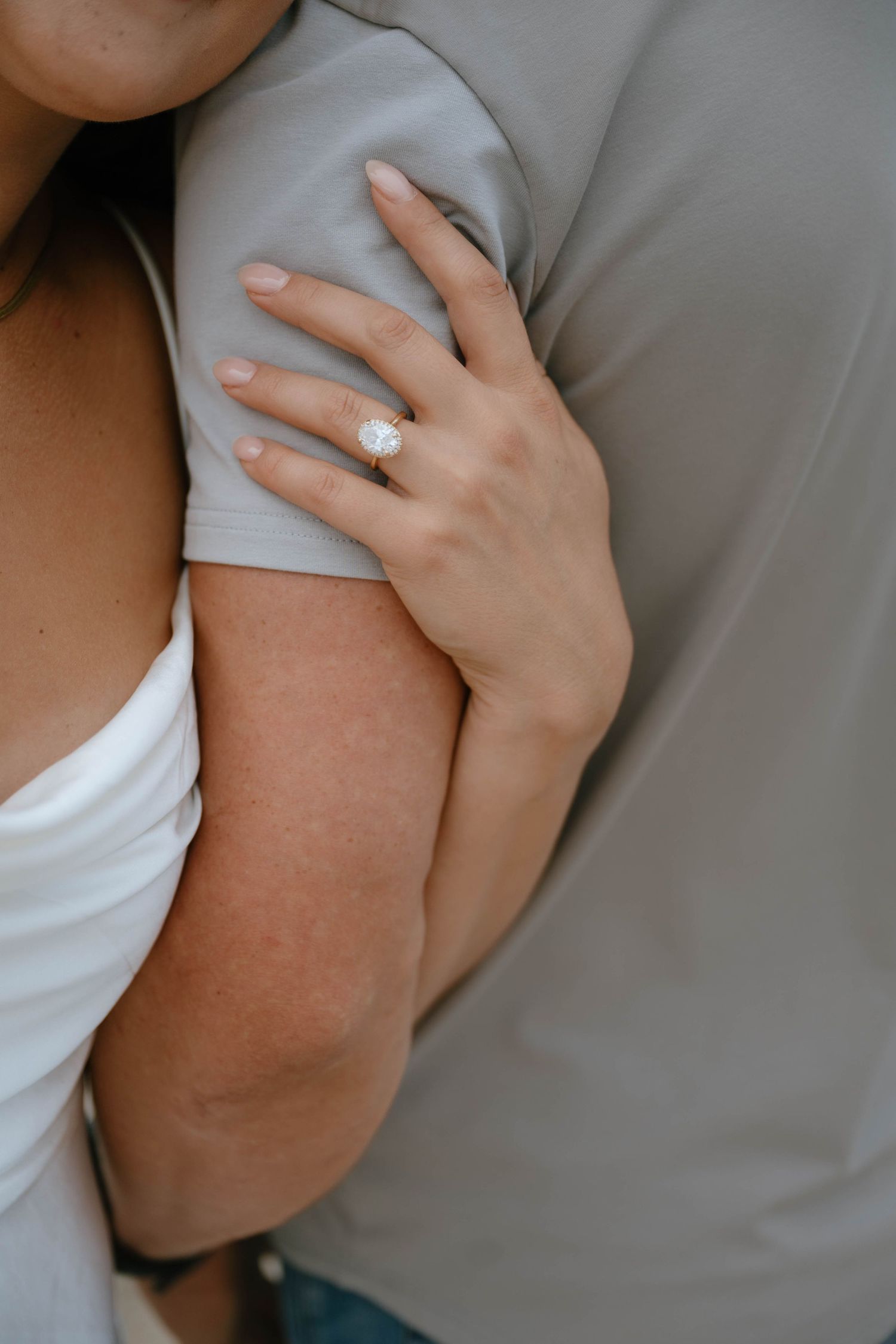 Close-up of a woman's hand with a large diamond engagement ring resting on a man's shoulder.