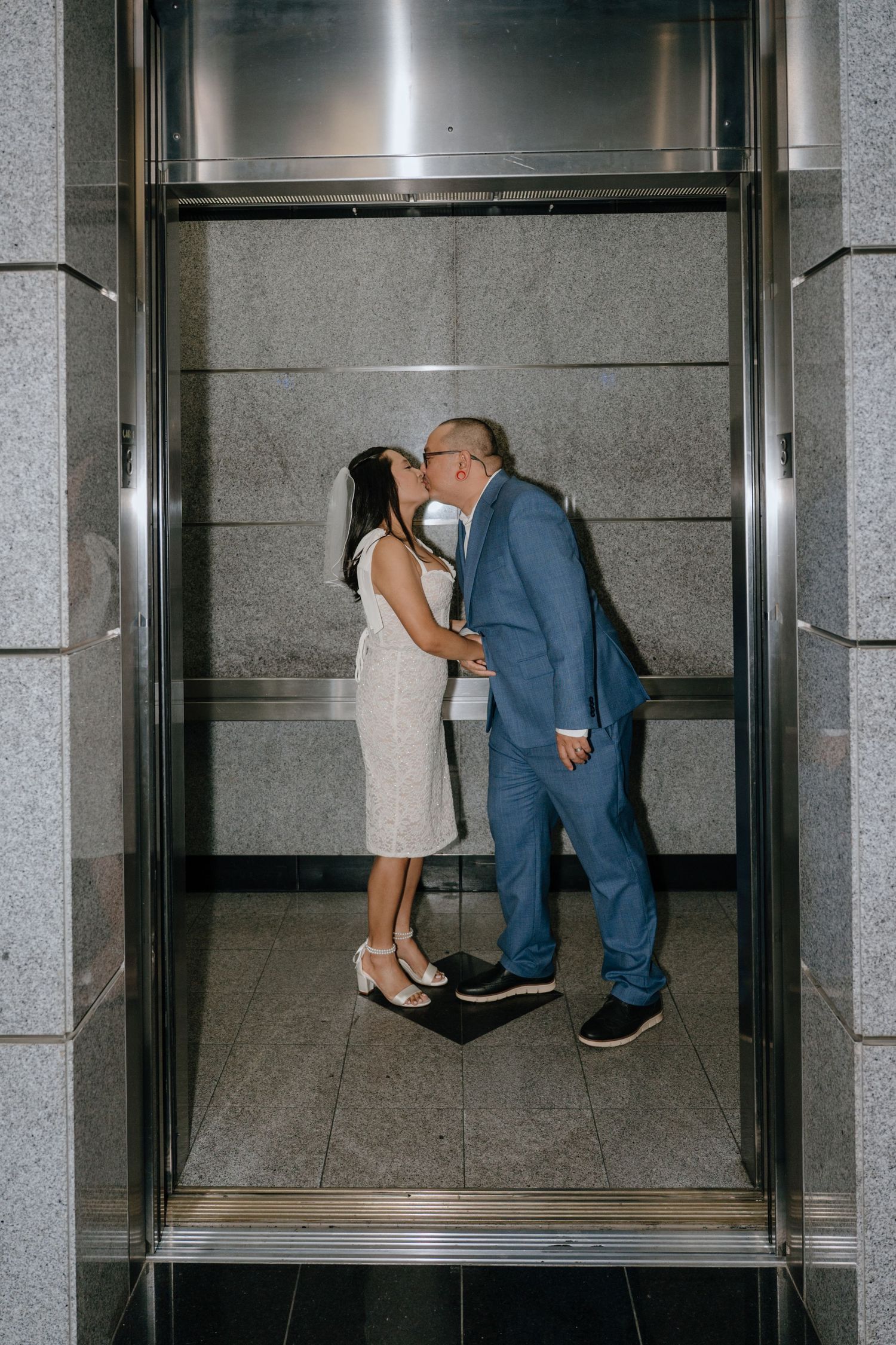 Bride and groom sharing a kiss inside an elevator on their wedding day.