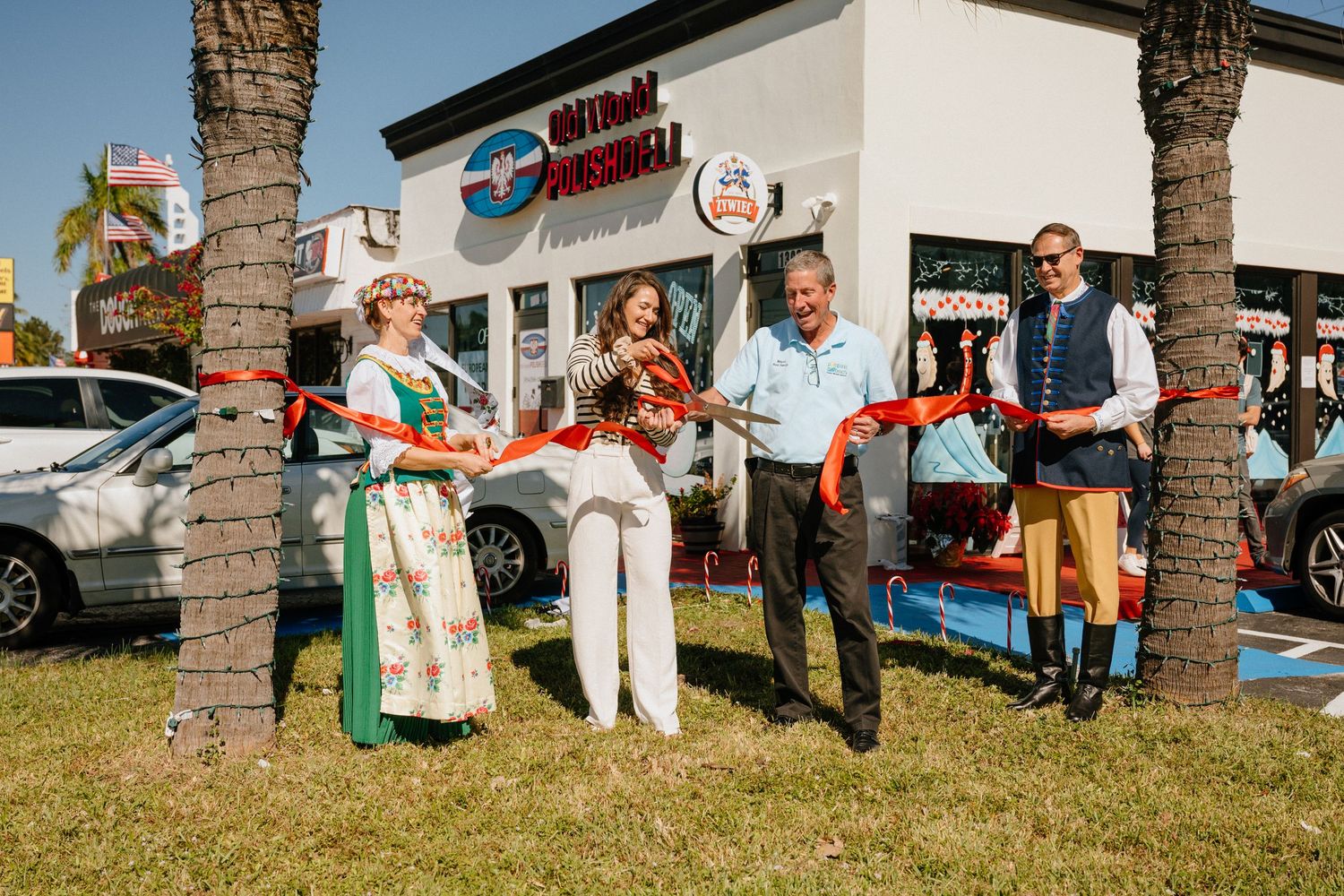 Four people celebrating a ribbon cutting ceremony at Old World Polish Deli, one wearing traditional Polish folk costume.