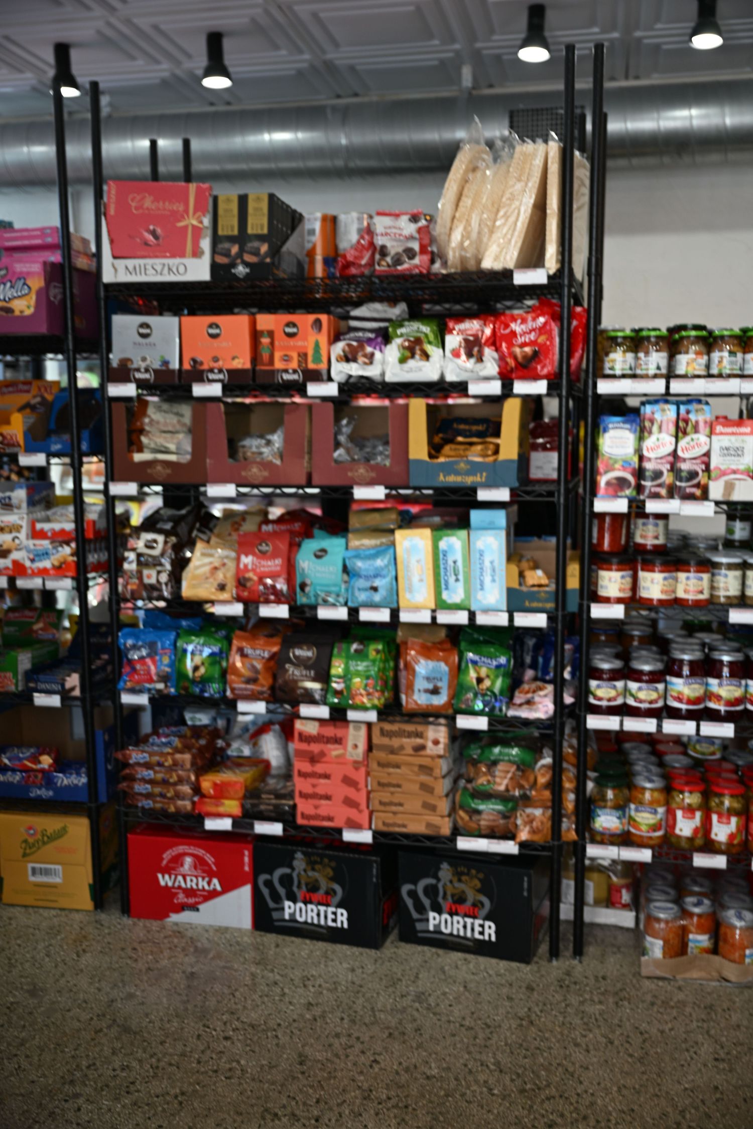Grocery store shelf stocked with Polish food products including Warka and Porter beer and assorted snacks.