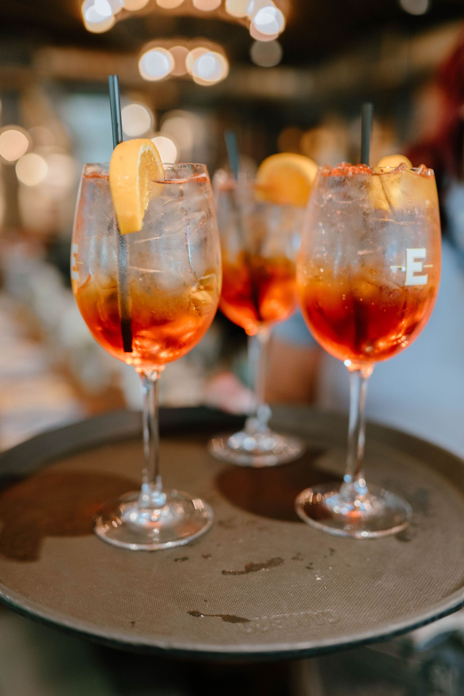 Three Aperol Spritz cocktails with orange slices and straws served on a dark tray at a baby shower.