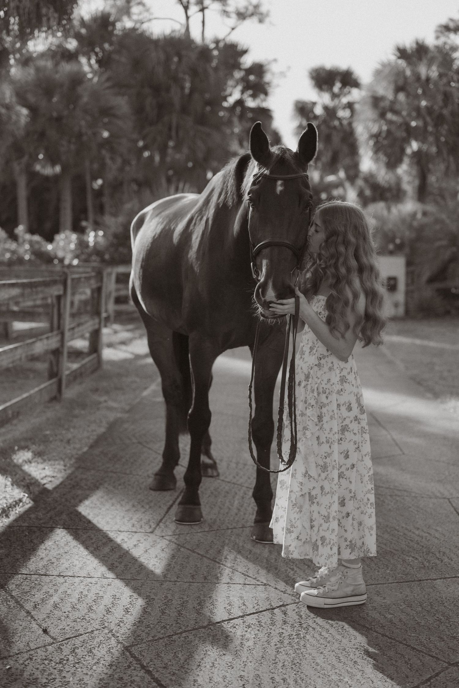Black and white photo of girl in floral dress sharing gentle moment with bay horse.