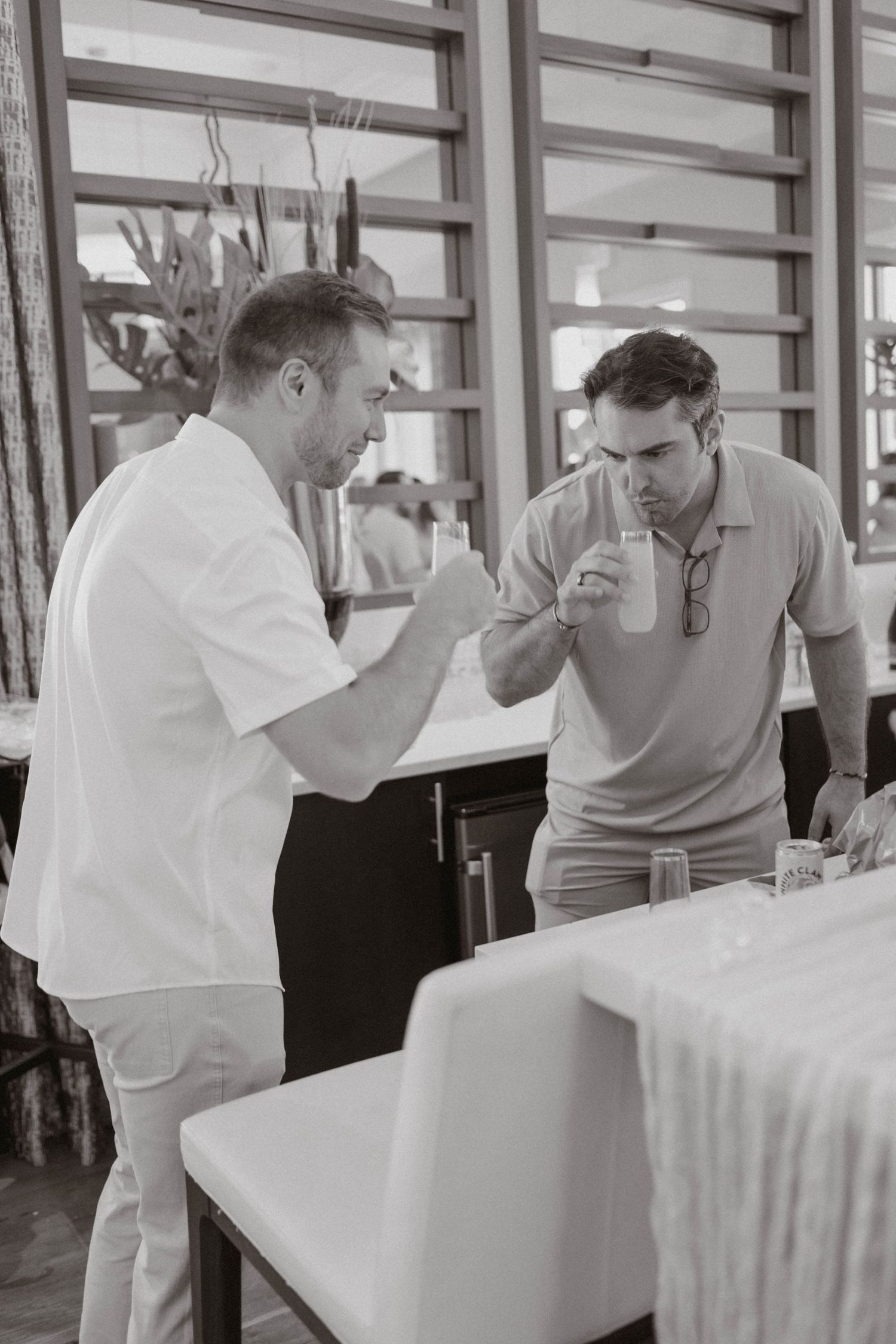 Black and white photo of two men examining something on a table in a bright restaurant setting.
