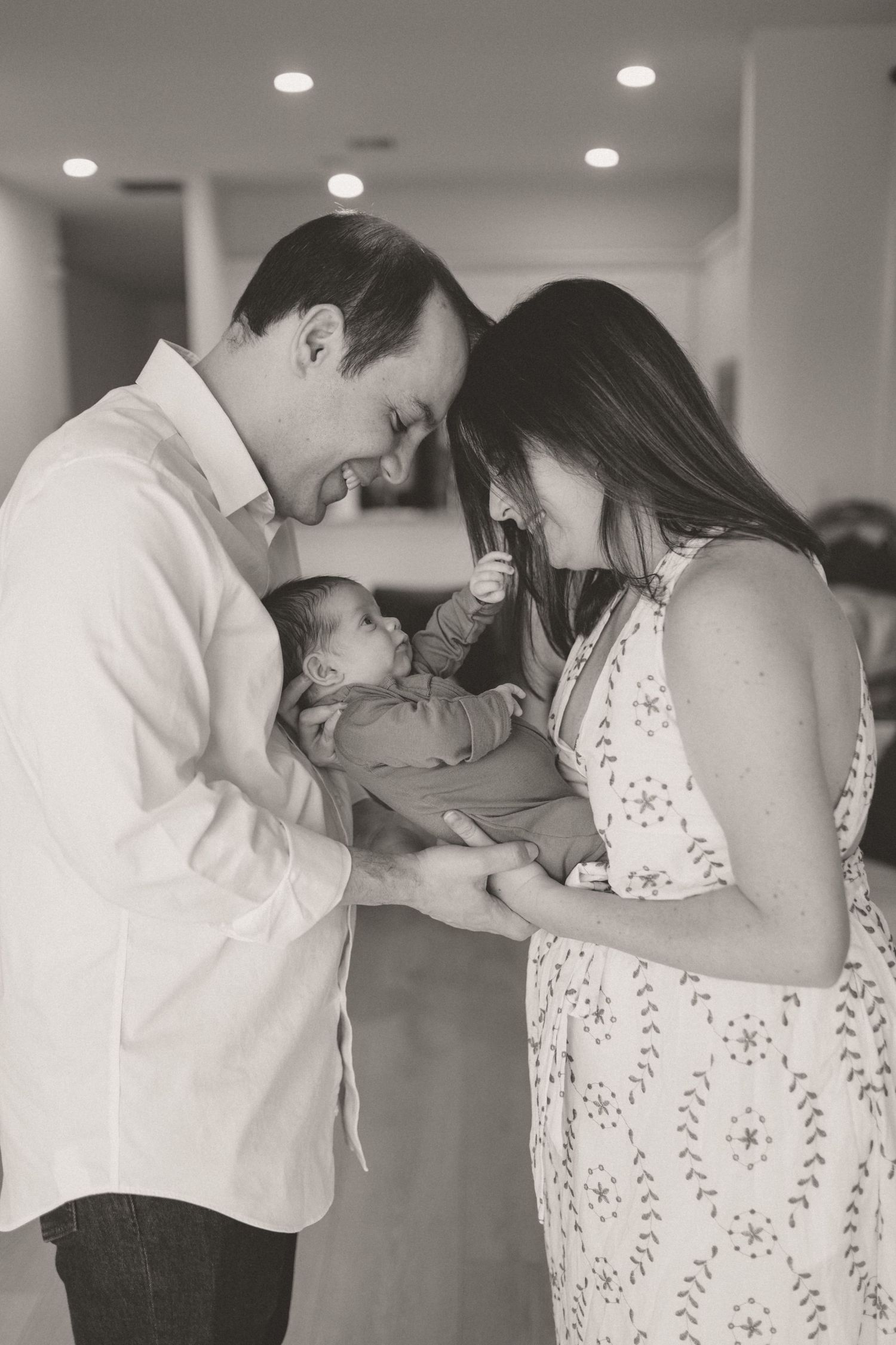 Black and white photo of smiling parents cradling their newborn baby together indoors.