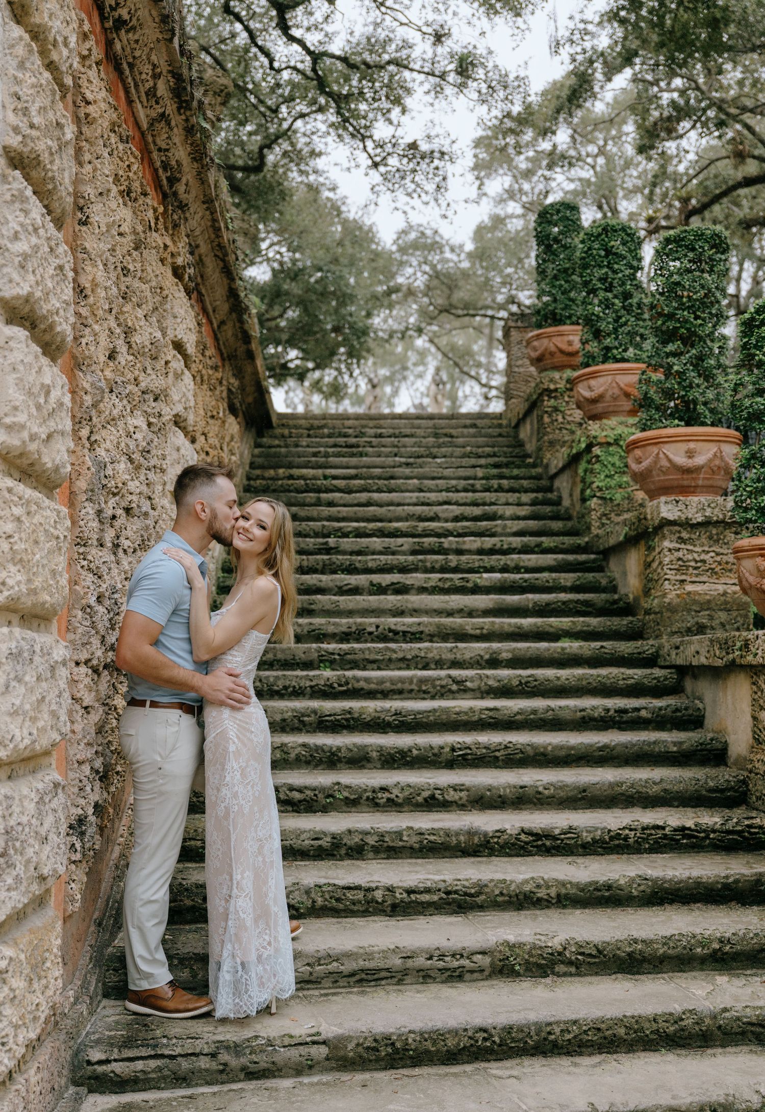 Couple sharing a kiss beside a stone staircase at a historic garden estate.