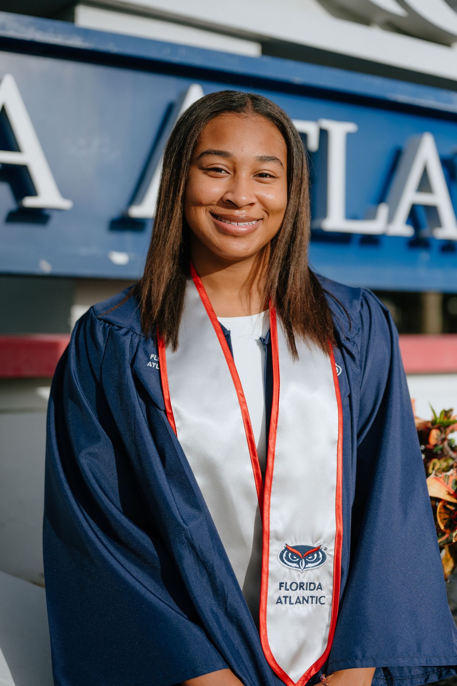 Smiling FAU graduate in navy gown with Florida Atlantic white stole and red lanyard.