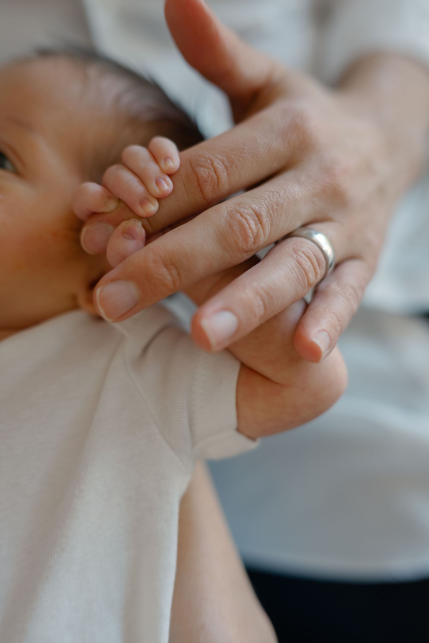 Newborn baby's tiny hand gripping a parent's finger wearing a silver ring.