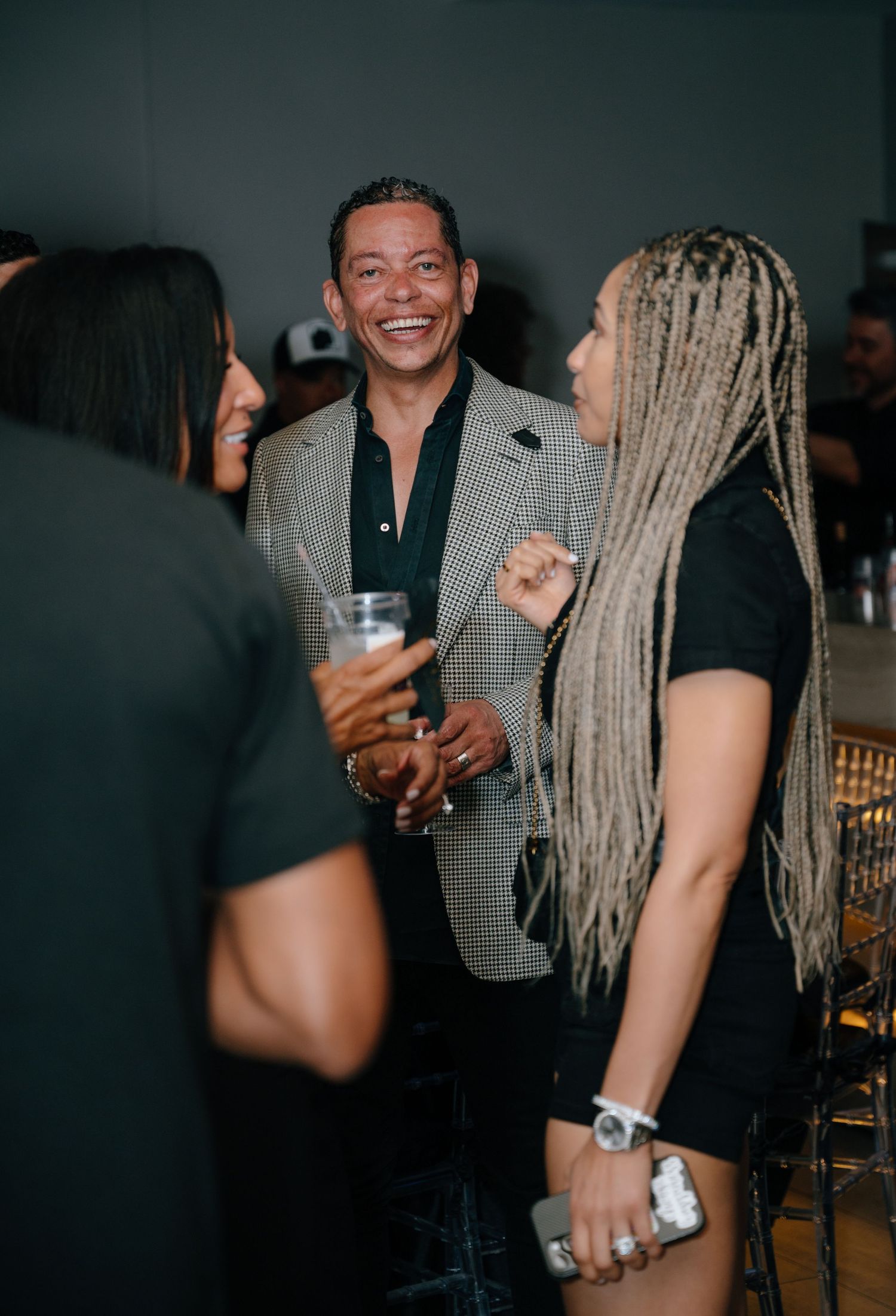 Man in checkered blazer laughing with guests while holding drink at a 40th birthday party.