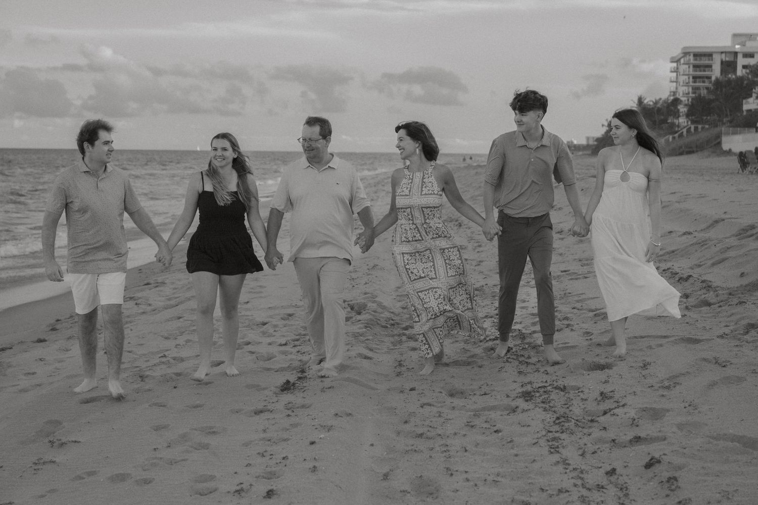 Black and white photo of six family members walking and laughing together along a sandy beach.