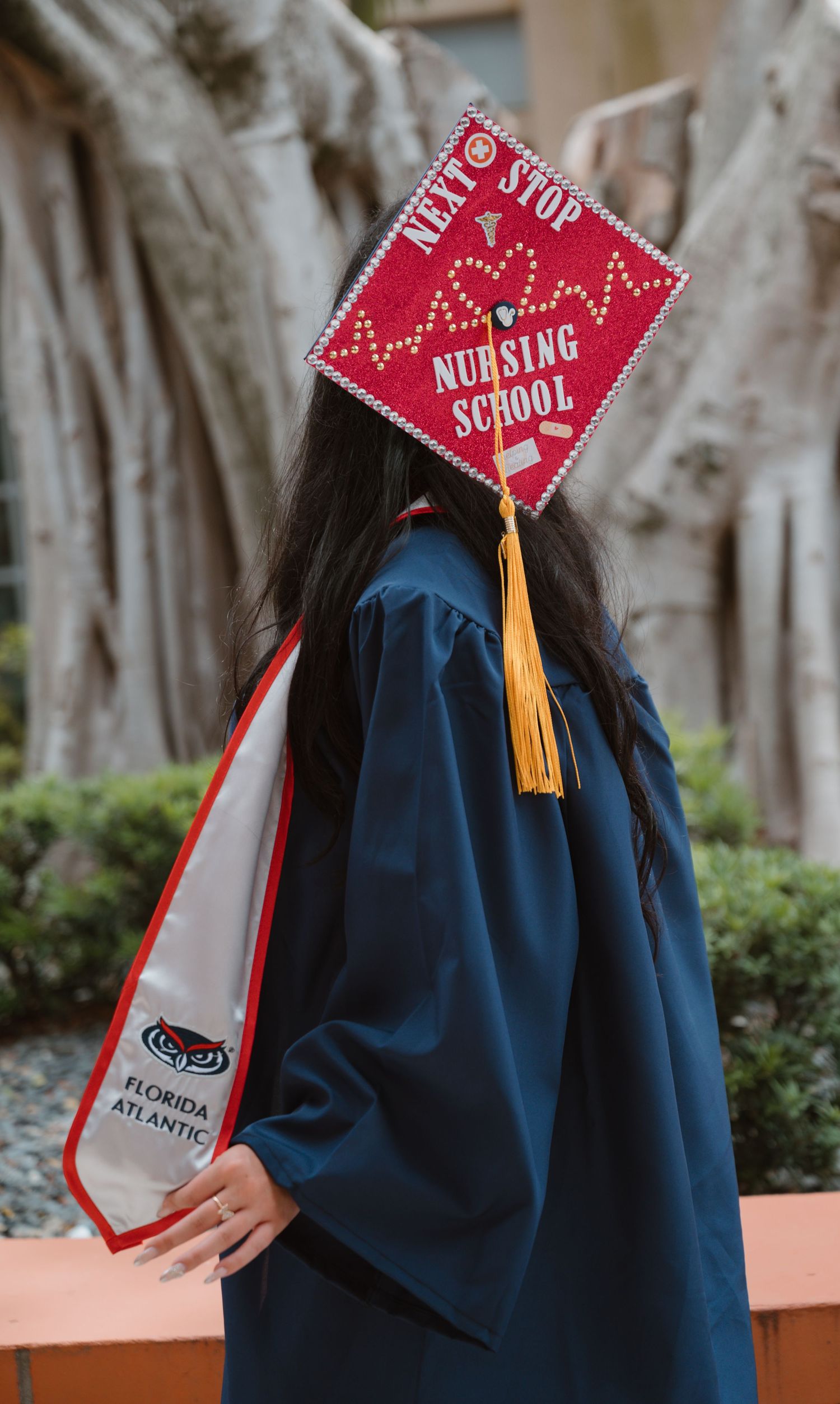 FAU nursing school graduate displays decorated red mortarboard reading Next Stop Nursing School.