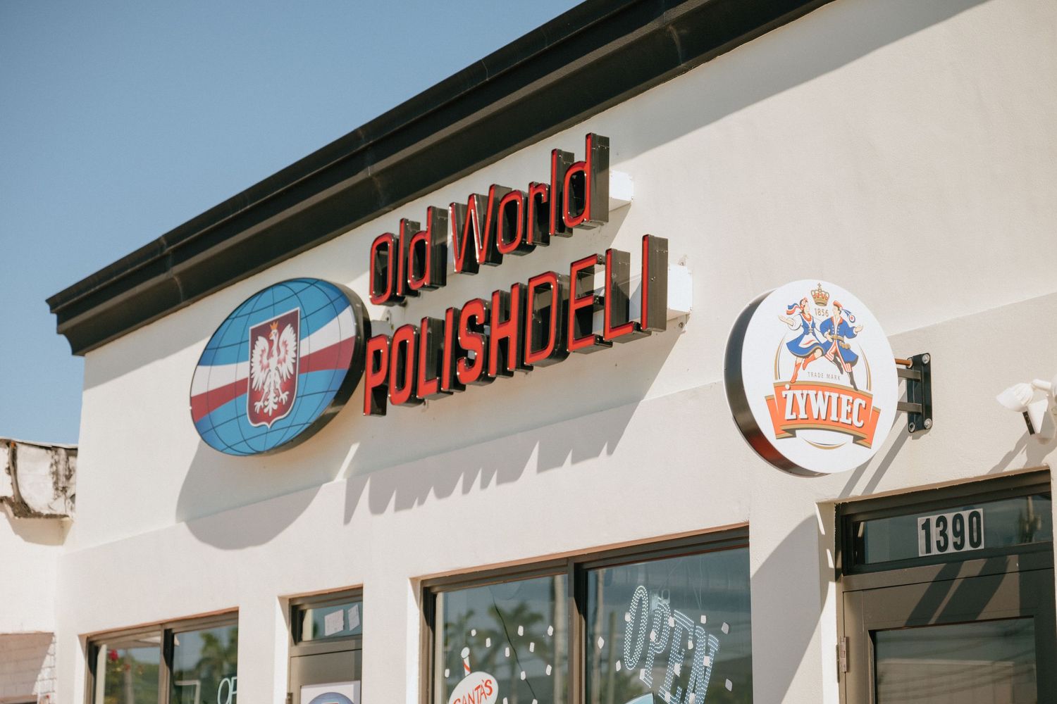 Exterior sign of Old World Polish Deli building featuring Polish eagle logo and Zywiec beer sign on white wall.