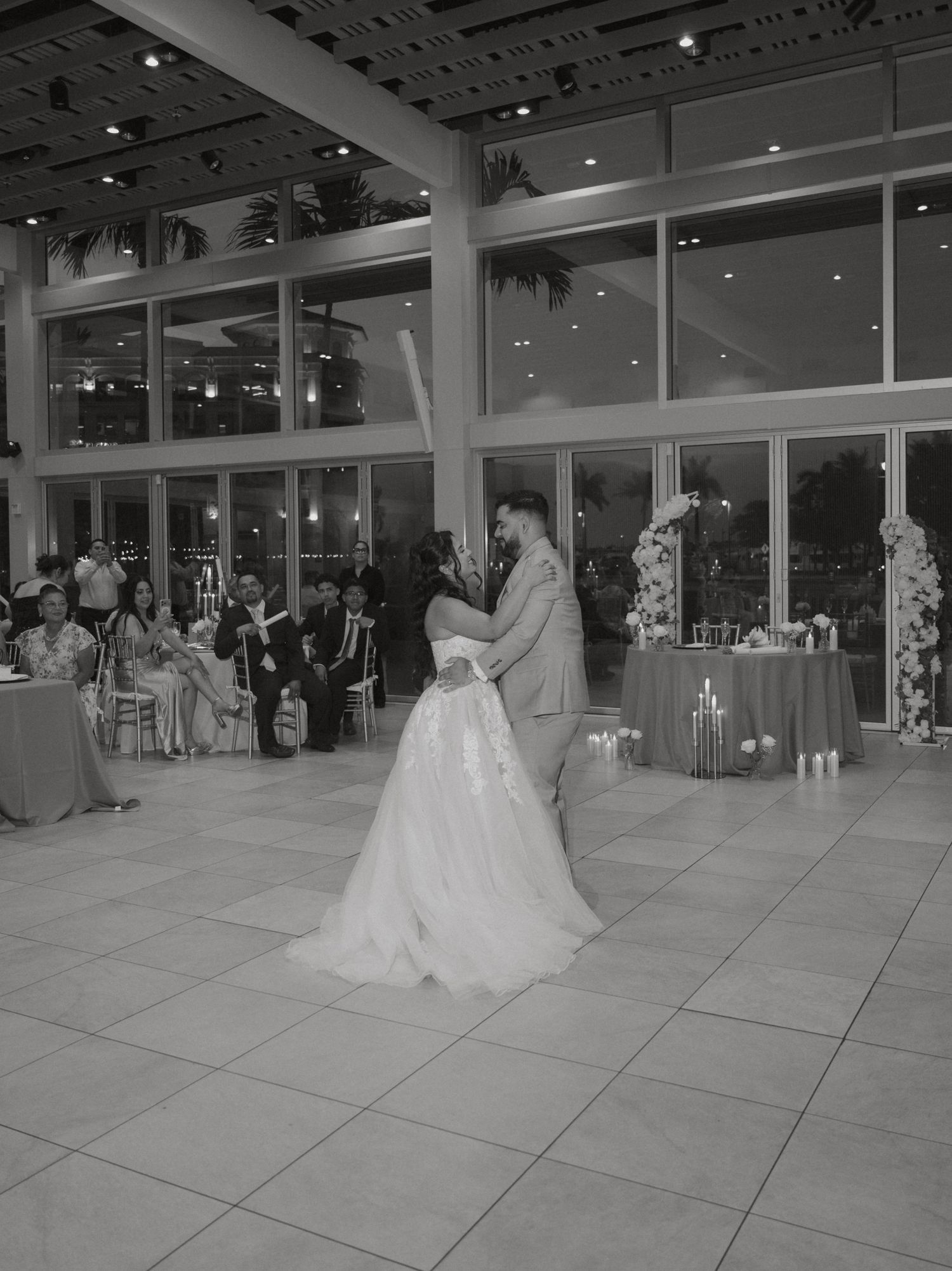 Bride and groom share their first dance in an elegant glass-walled ballroom reception venue.