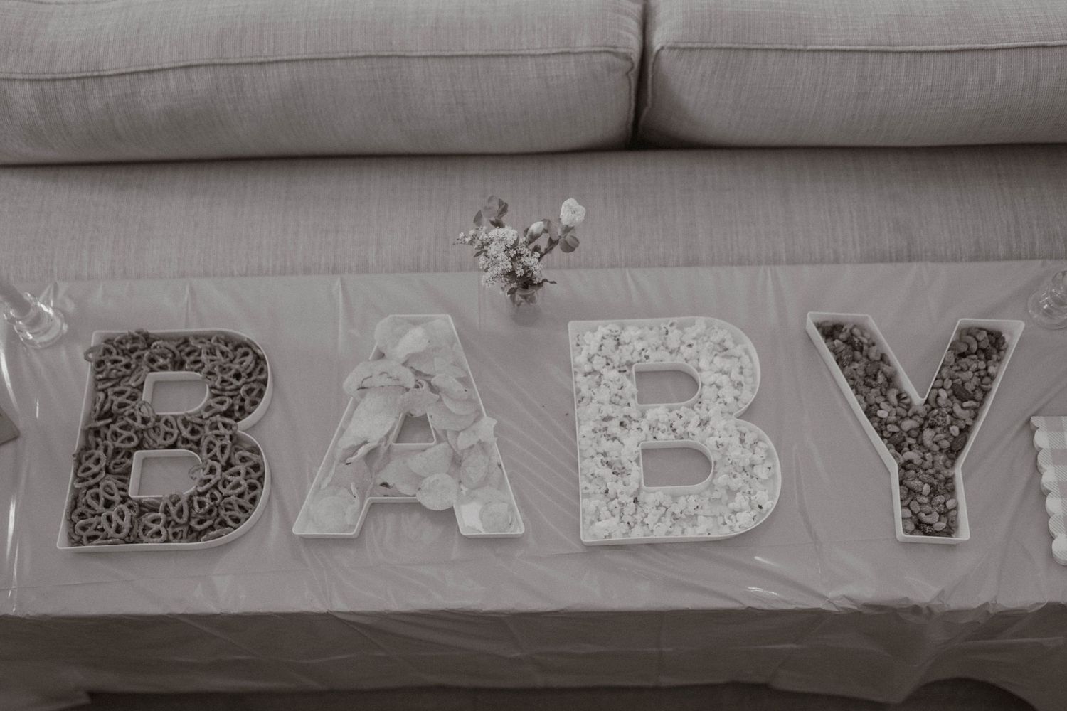 Decorative white lace BABY letters arranged on a gray couch with small flowers.