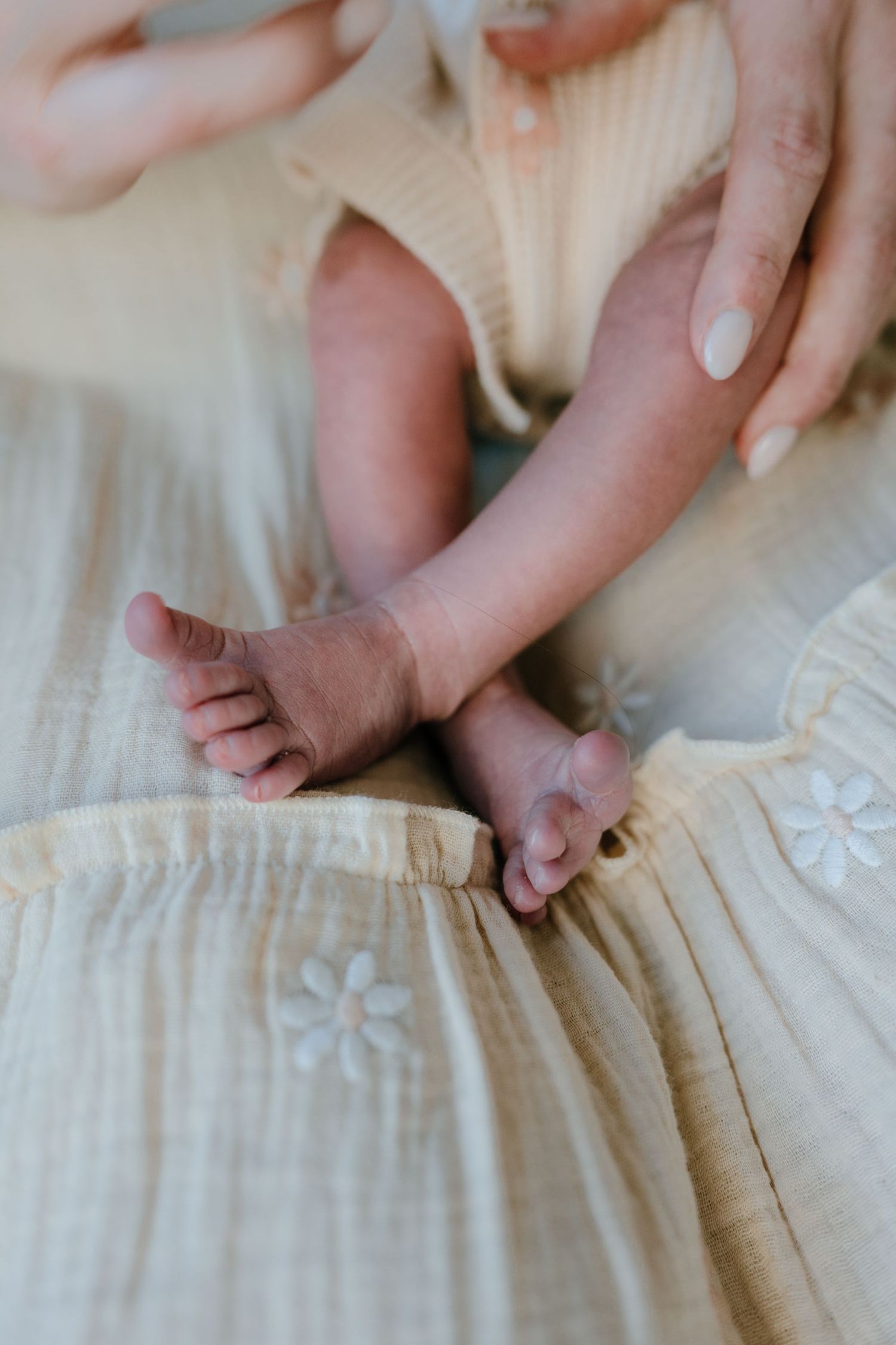 Close-up of tiny newborn baby feet resting on mother's floral embroidered skirt.
