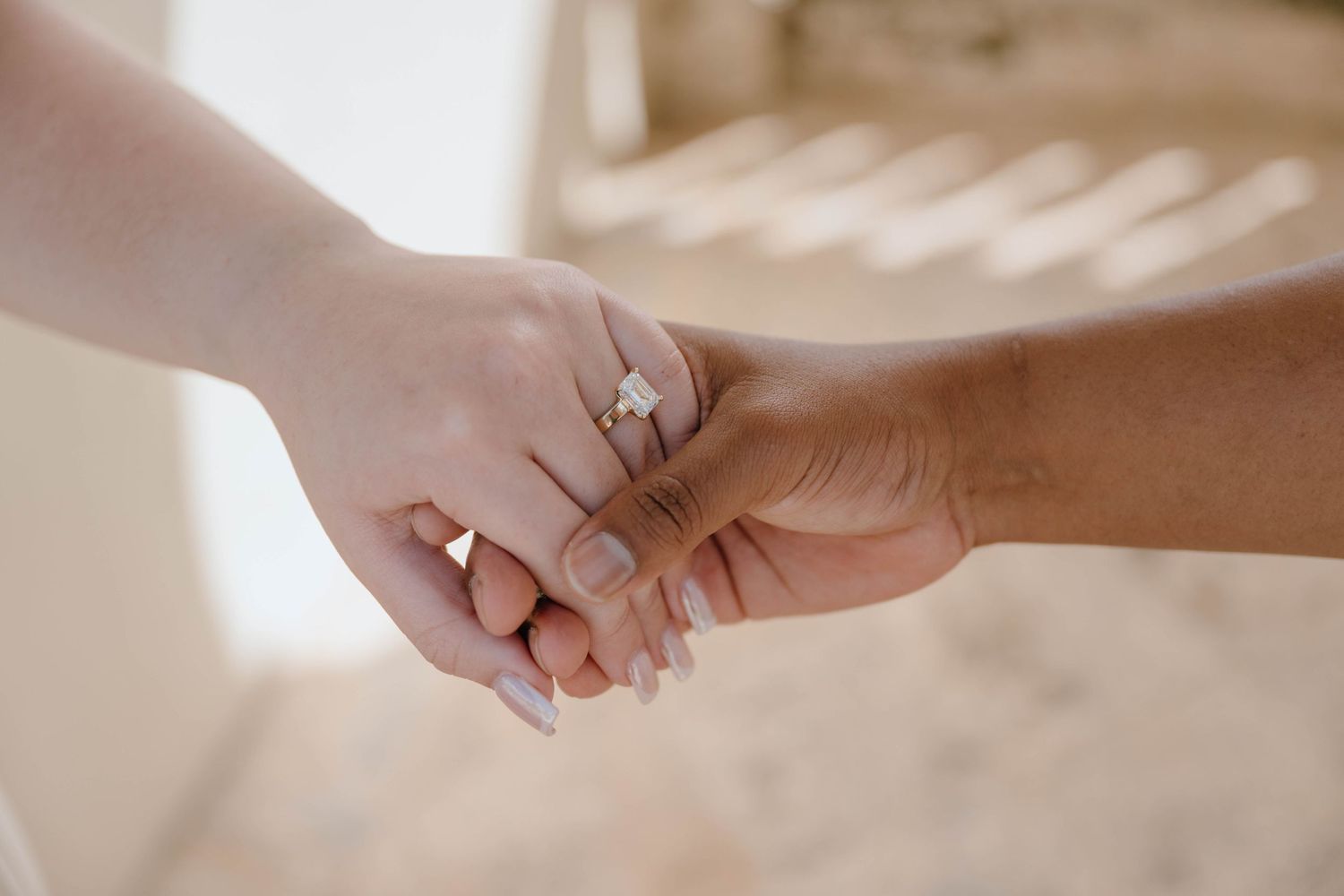 Close-up of couple holding hands showing emerald cut diamond engagement ring after proposal.