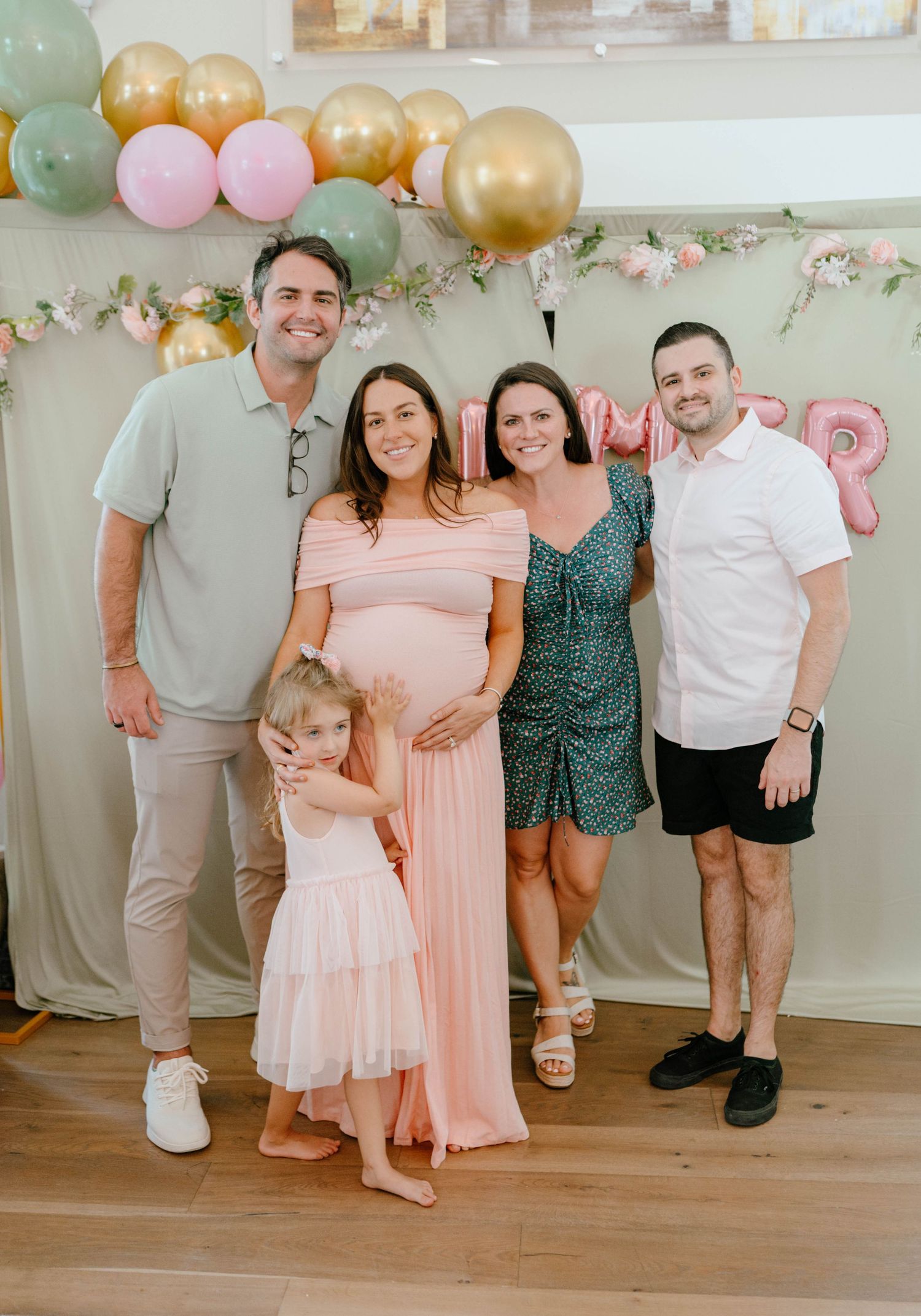A family group poses together at a colorful balloon-decorated baby shower backdrop.